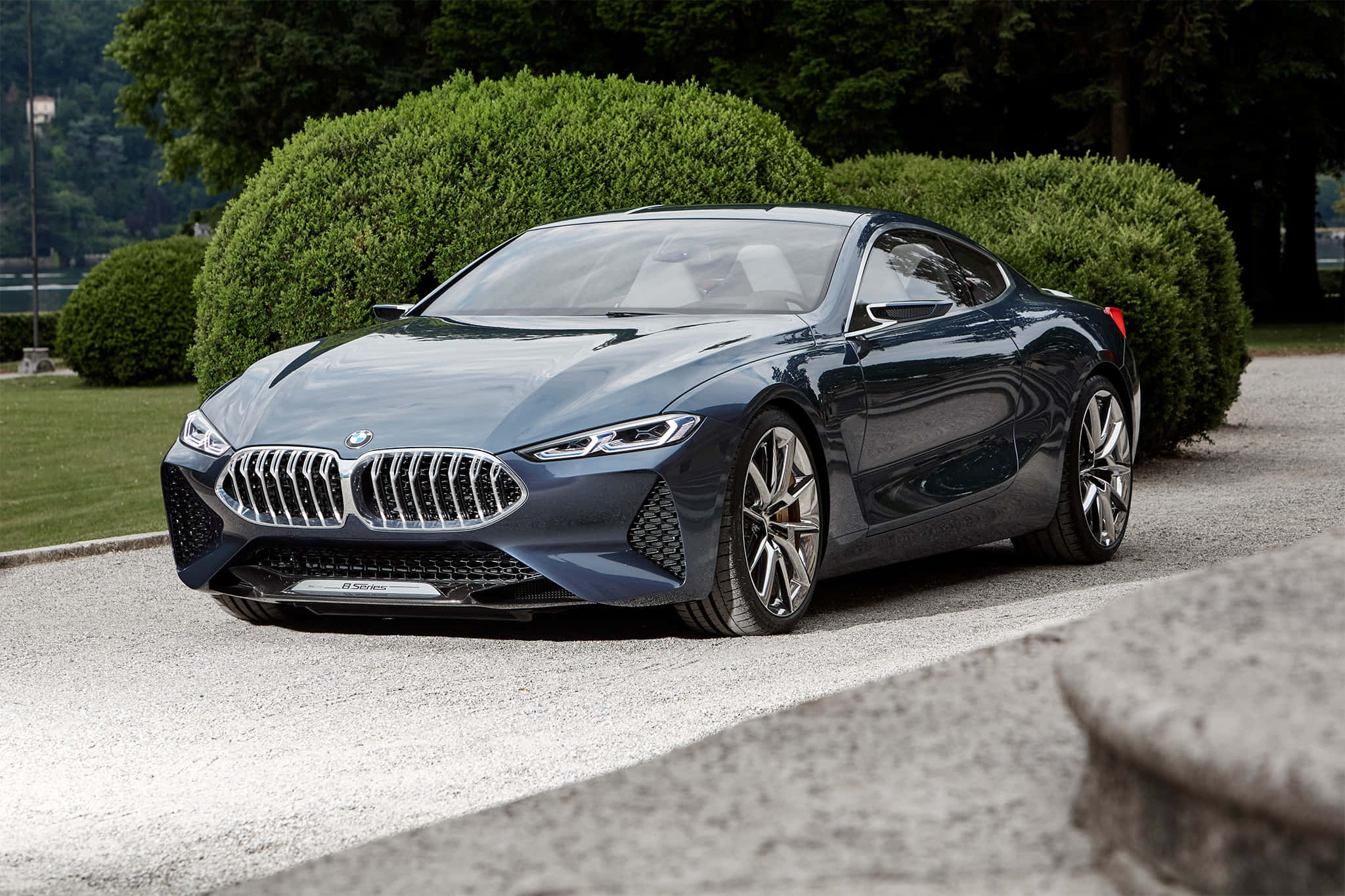 Bmw 8 Series 桌布 壁紙 — 一輛時尚的深藍色BMW概念車在日光下閃耀，停在碎石路上，旁邊是修剪整齊的綠色樹籬。