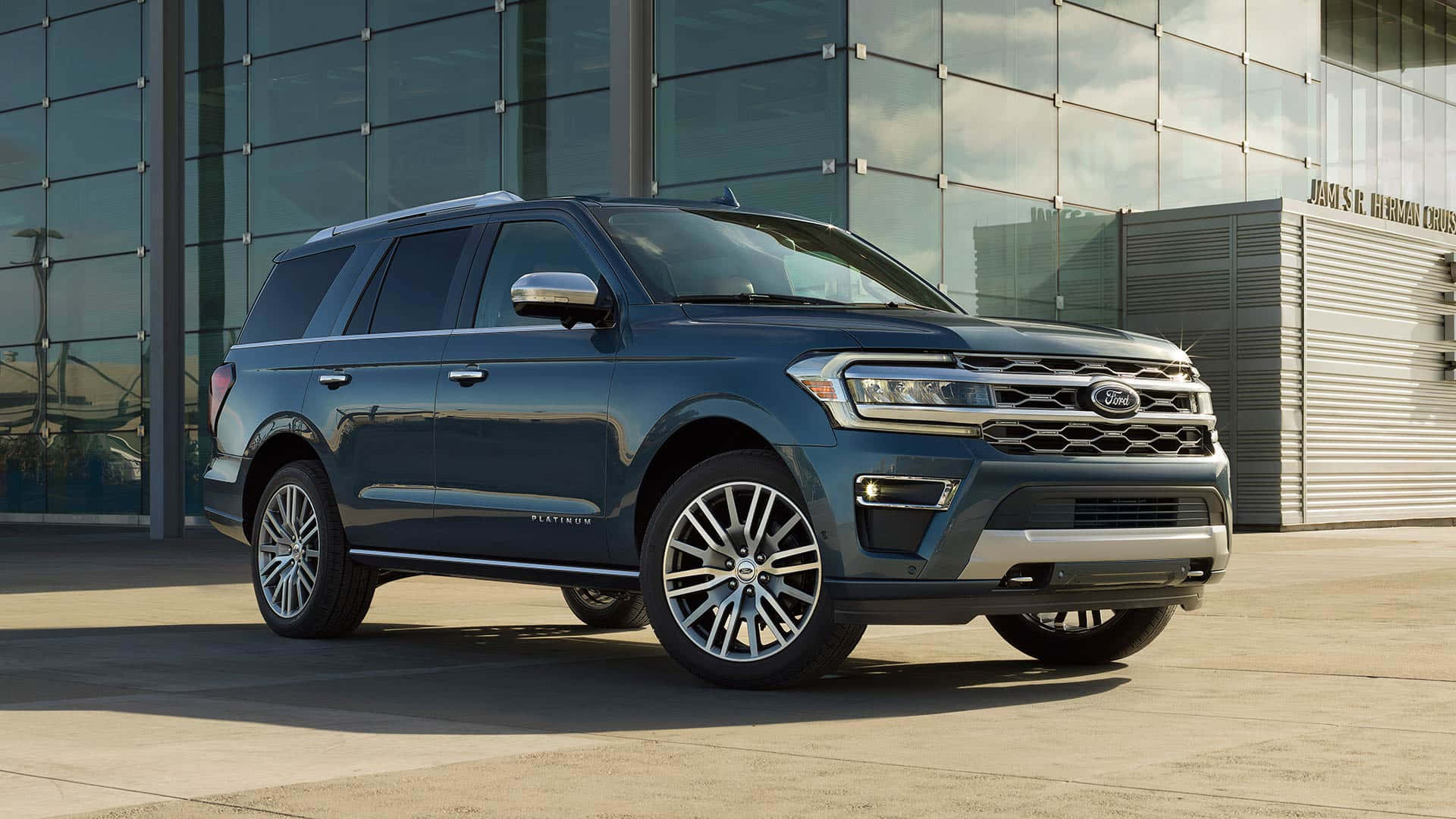 Ford Expedition 桌布 壁紙 — 一輛時尚的深藍色Ford Expedition Platinum SUV在明亮的日光下停放在現代玻璃建築前。