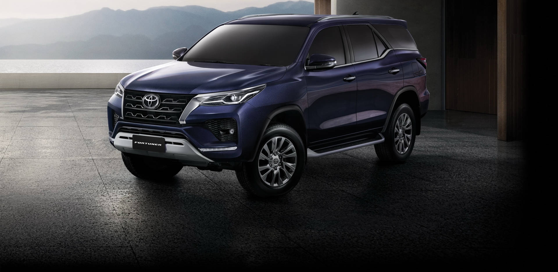 深藍色豐田 Fortuner SUV 停放在混凝土平台上，俯瞰山脈和海洋。 — Toyota Supra Mk4 壁紙