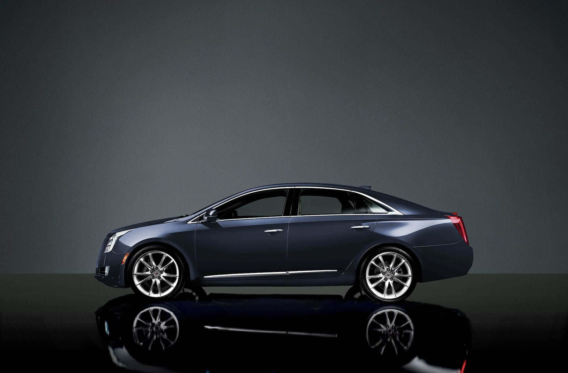Cadillac Xts 桌布 壁紙 — 一輛時尚的深藍色豪華轎車側面立於反光黑色表面上，背景為柔和的灰色攝影棚。