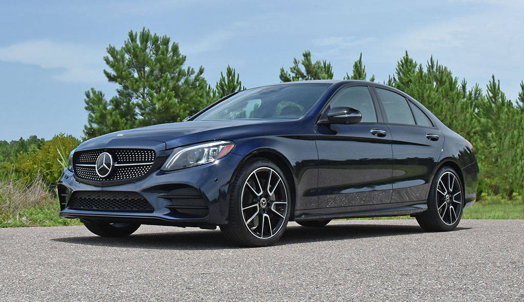 Mercedes Benz C300 桌布 壁紙 — 一輛時尚的深藍色賓士C-Class轎車停泊在碎石上，背景有綠樹和晴朗的藍天。