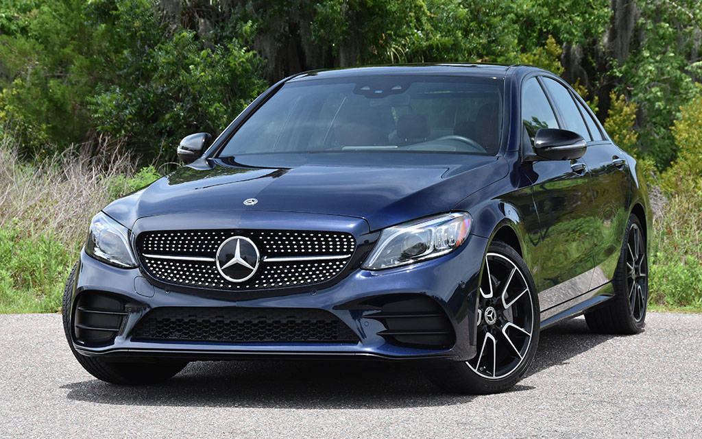 Mercedes Benz C300 桌布 壁紙 — 一輛時尚的深藍色賓士轎車在明亮的日光下閃閃發光，停在柏油路上，背後是茂密的綠色樹葉。