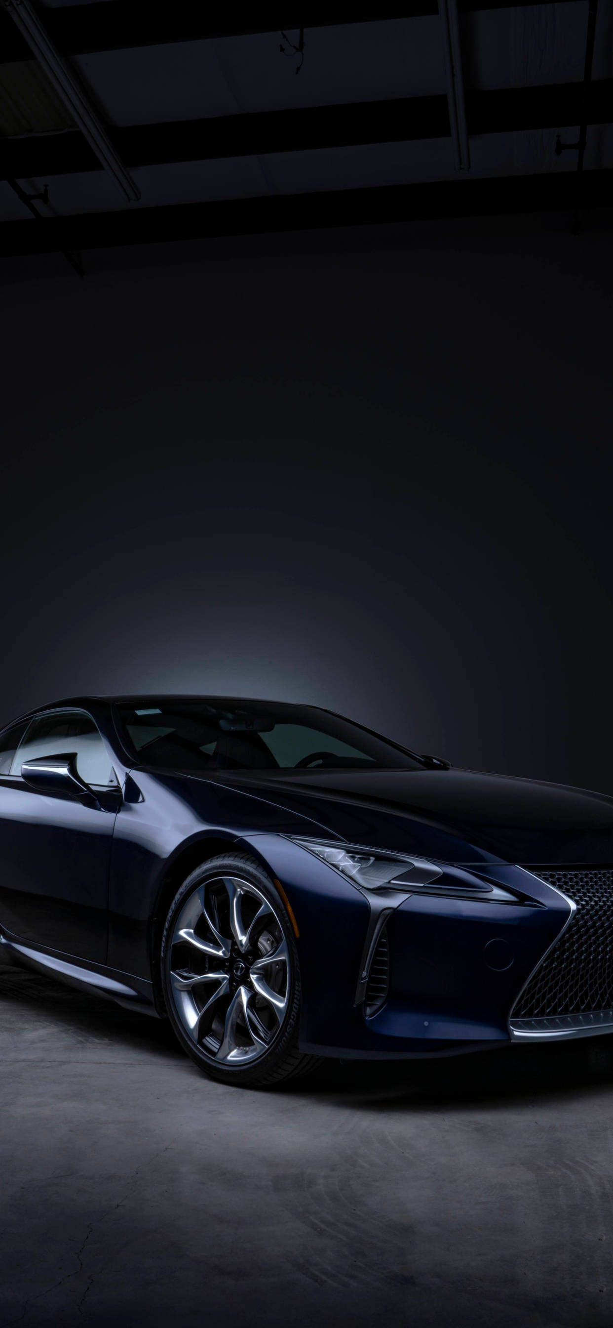 lexus iPhone 桌布 壁紙 — 一輛時尚的深藍色跑車在極簡工業車庫中，於戲劇性聚光燈下閃耀。