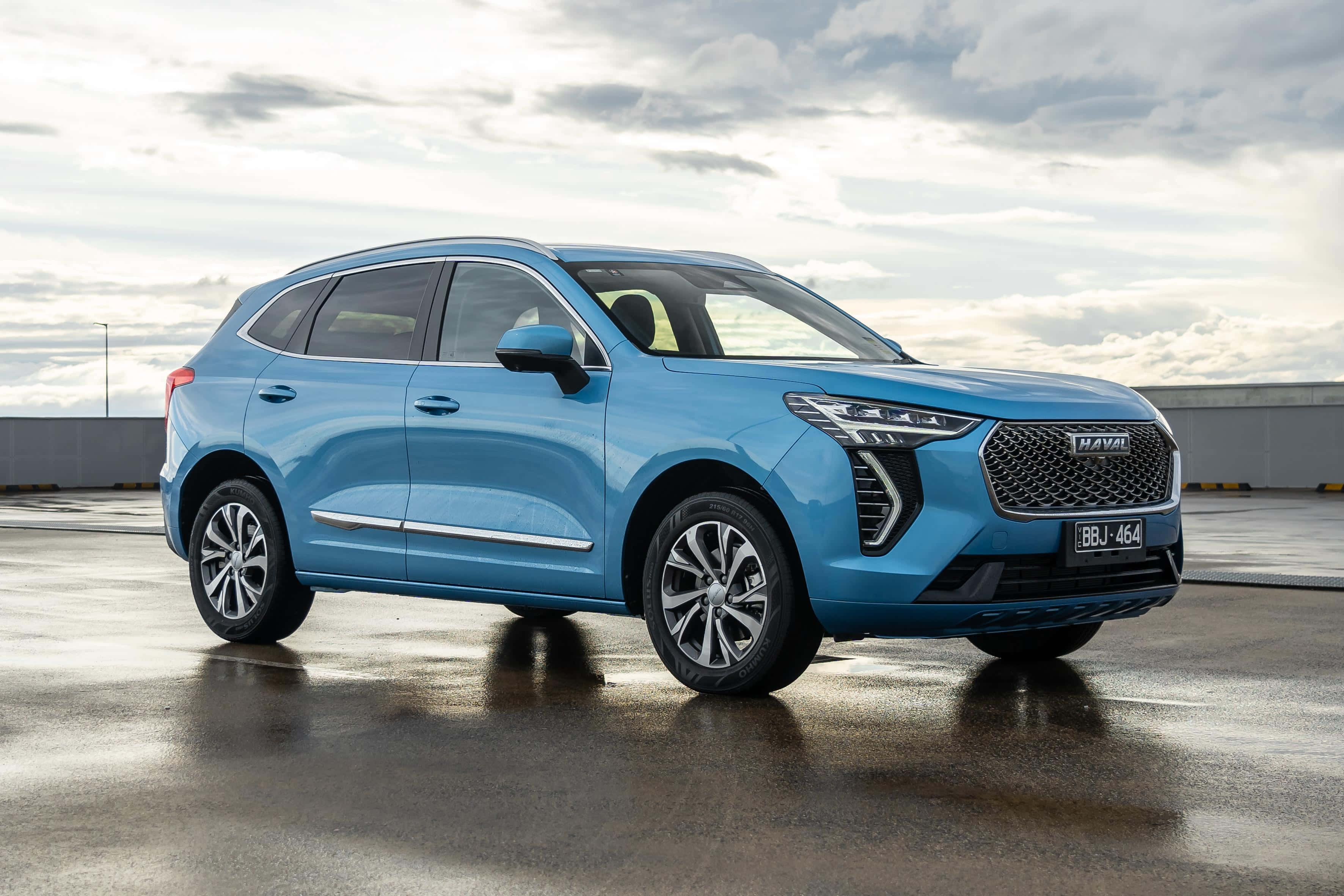 Haval 桌布 壁紙 — 一輛時尚的淺藍色Haval SUV在潮濕的停車場上閃閃發光，天空多雲，倒影在路面上閃爍。