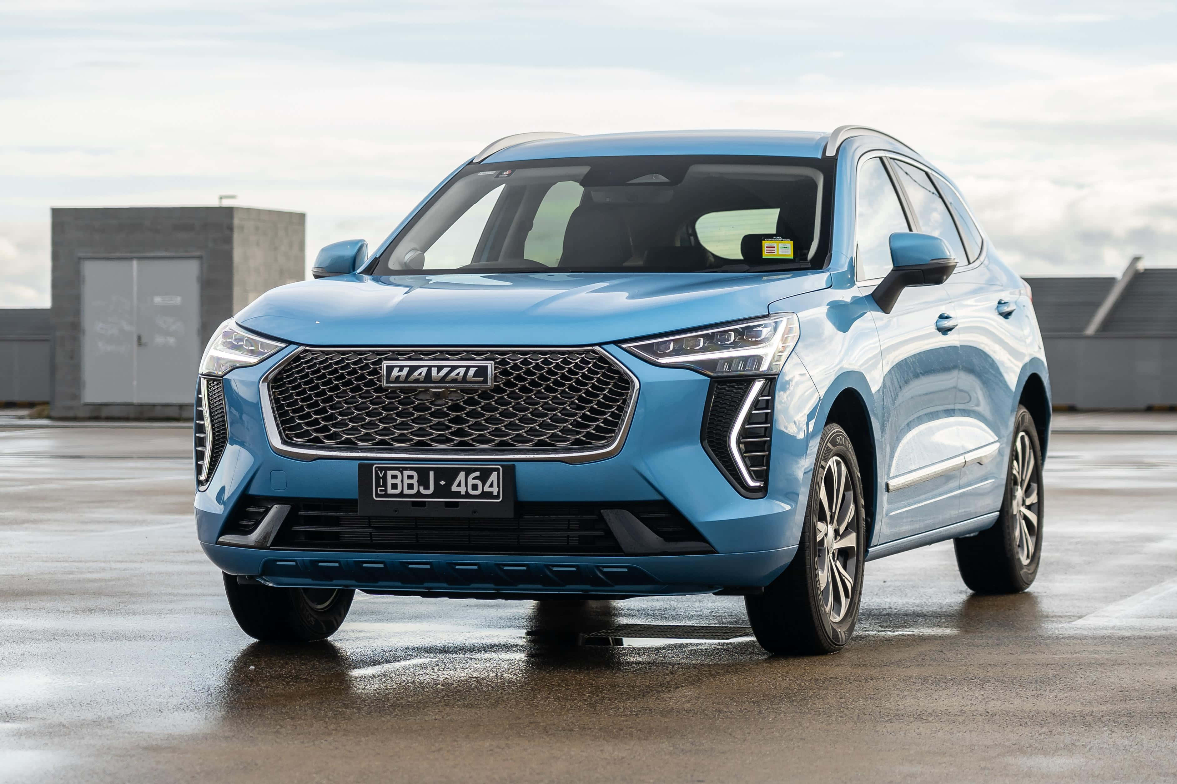 Haval 桌布 壁紙 — 一輛時尚的淺藍色哈弗SUV停放在濕漉漉的混凝土表面上，背景是現代工業建築，天空多雲。