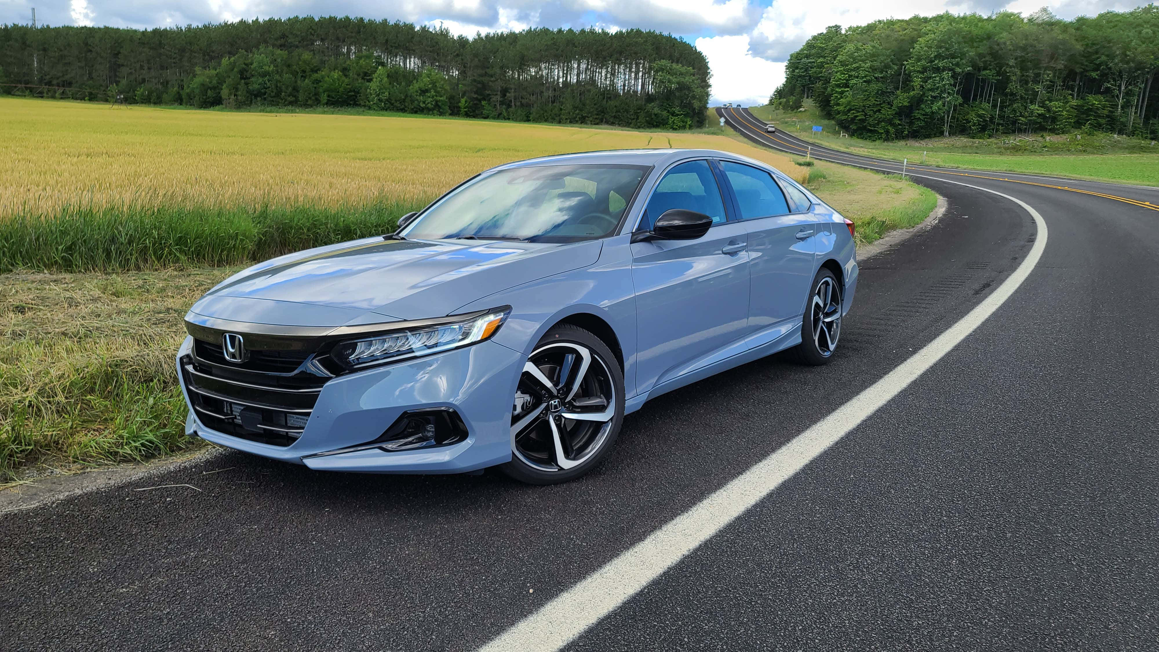 Honda Accord 桌布 壁紙 — 一輛時尚的淺藍色本田轎車停泊在蜿蜒的鄉村道路上，旁邊是金黃色的田野，天空部分多雲。