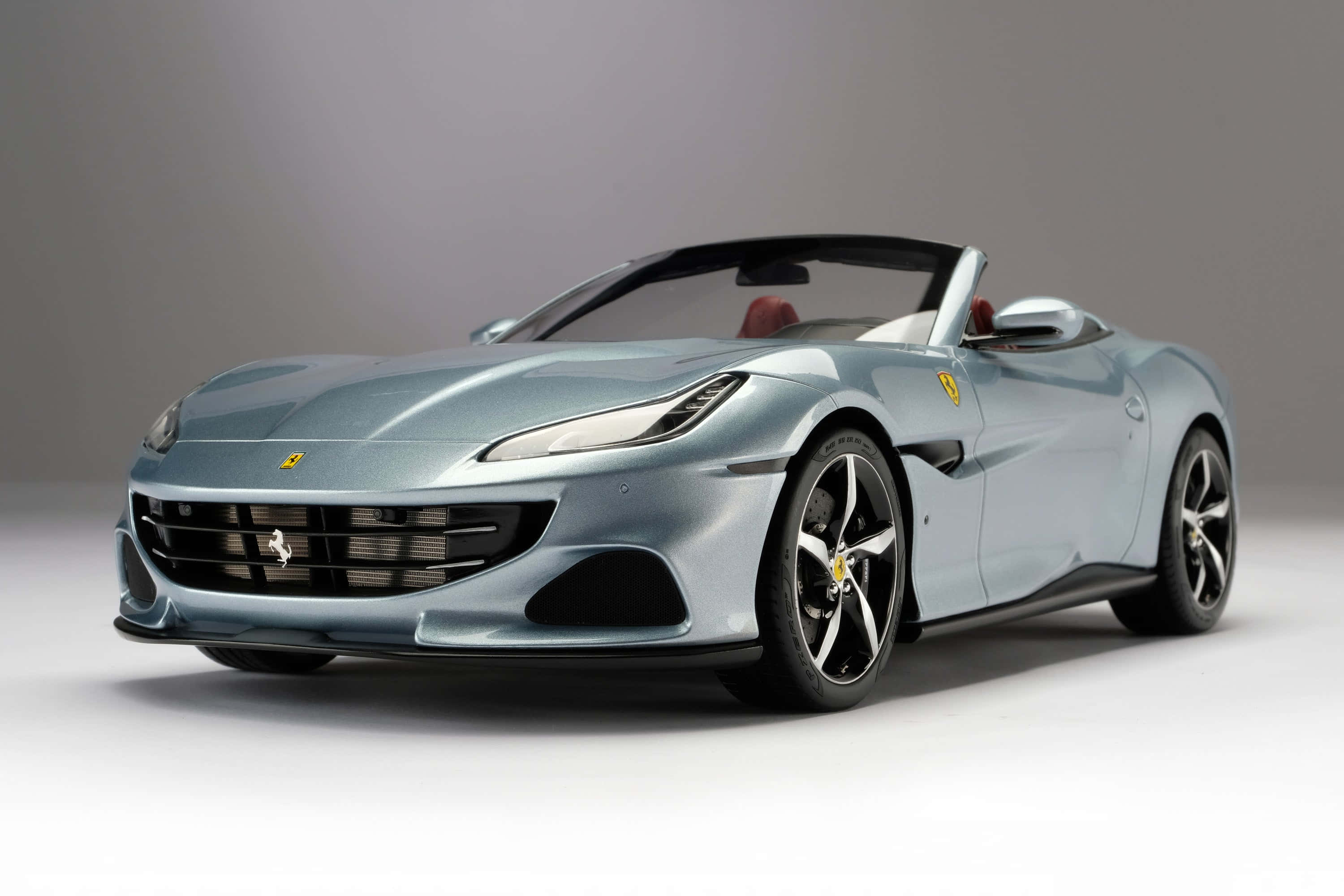 Ferrari Portofino 桌布 壁紙 — 一輛時尚的淺藍色法拉利敞篷跑車，帶有黑色飾邊和紅色座椅，在中性攝影棚背景下展示。
