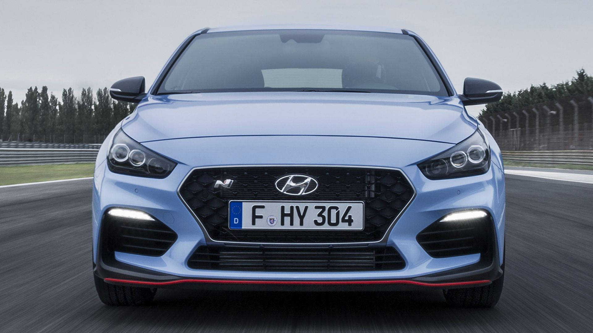 Hyundai 桌布 壁紙 — 一輛時尚的淺藍色現代N性能車在賽道上疾馳，帶有模糊的動感和紅色飾邊。
