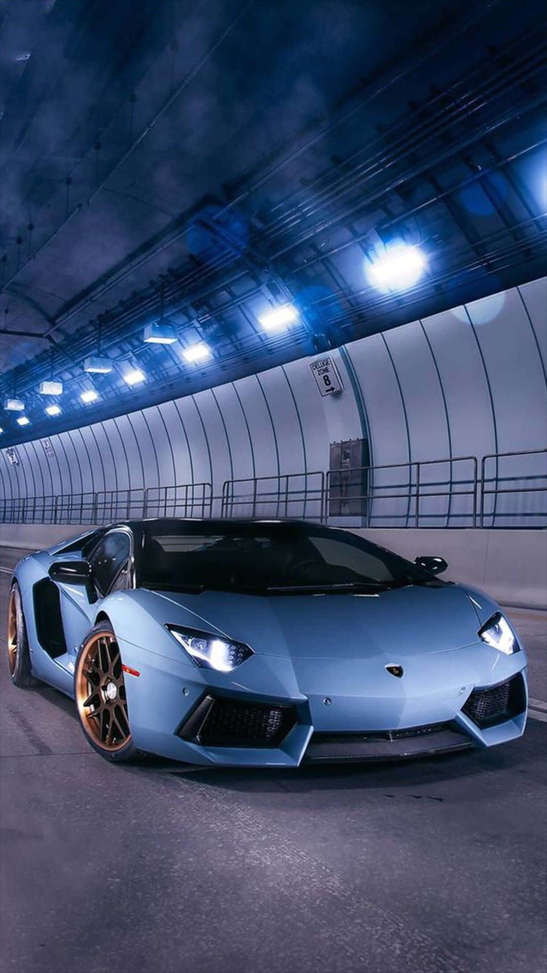電玩遊戲 桌布 壁紙 — 一輛時尚的淺藍色藍寶堅尼 Aventador 配金色輪圈，在頭頂藍色燈光照亮的昏暗隧道中滑行。