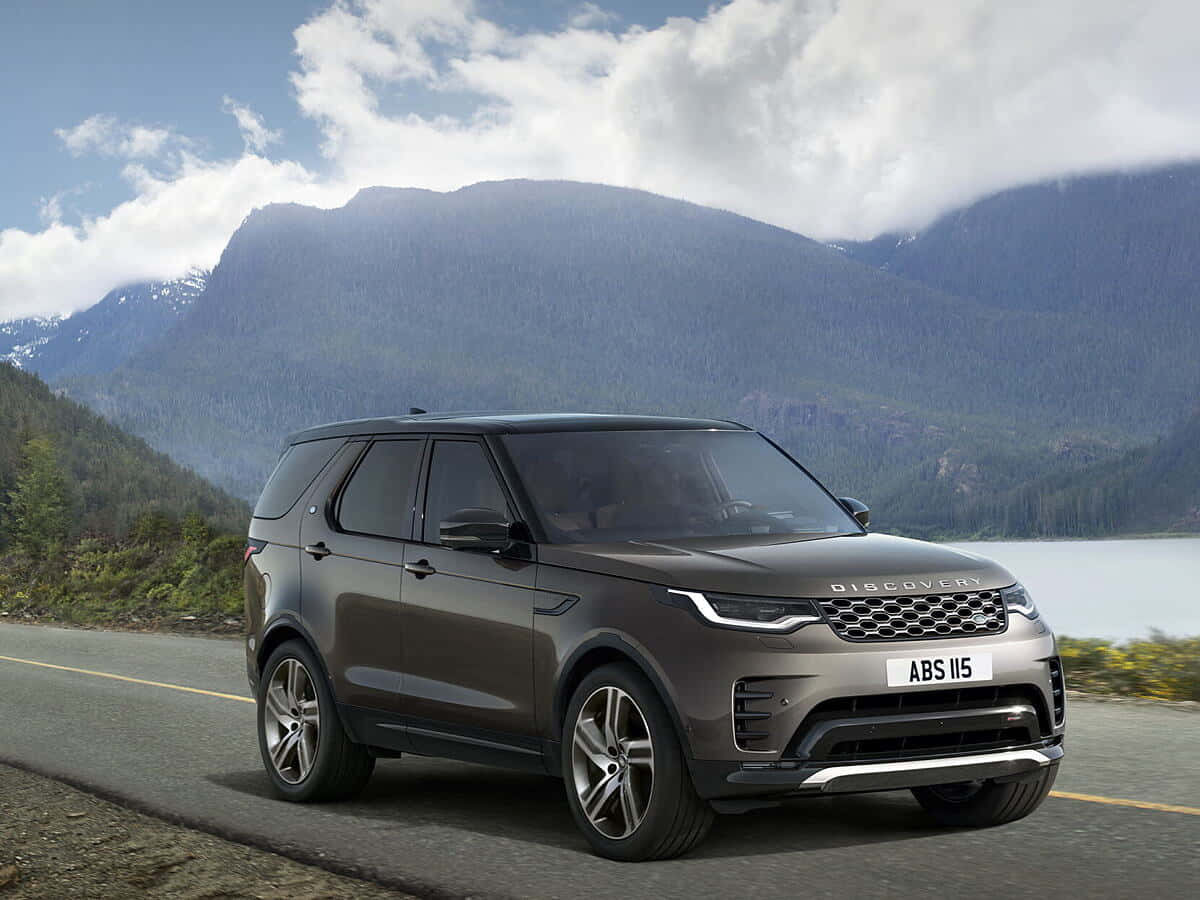 Land Rover Discovery 桌布 壁紙 — 一輛時尚的灰色 Land Rover Discovery 在陰天下行駛在湖邊的山路上。