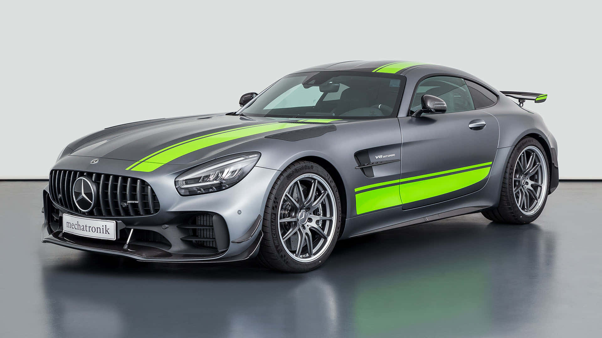汽車 桌布 壁紙 — 一輛時尚的灰色 Mercedes-AMG GT R 跑車，帶有鮮豔的綠色賽車條紋，在極簡風格的攝影棚中展示。