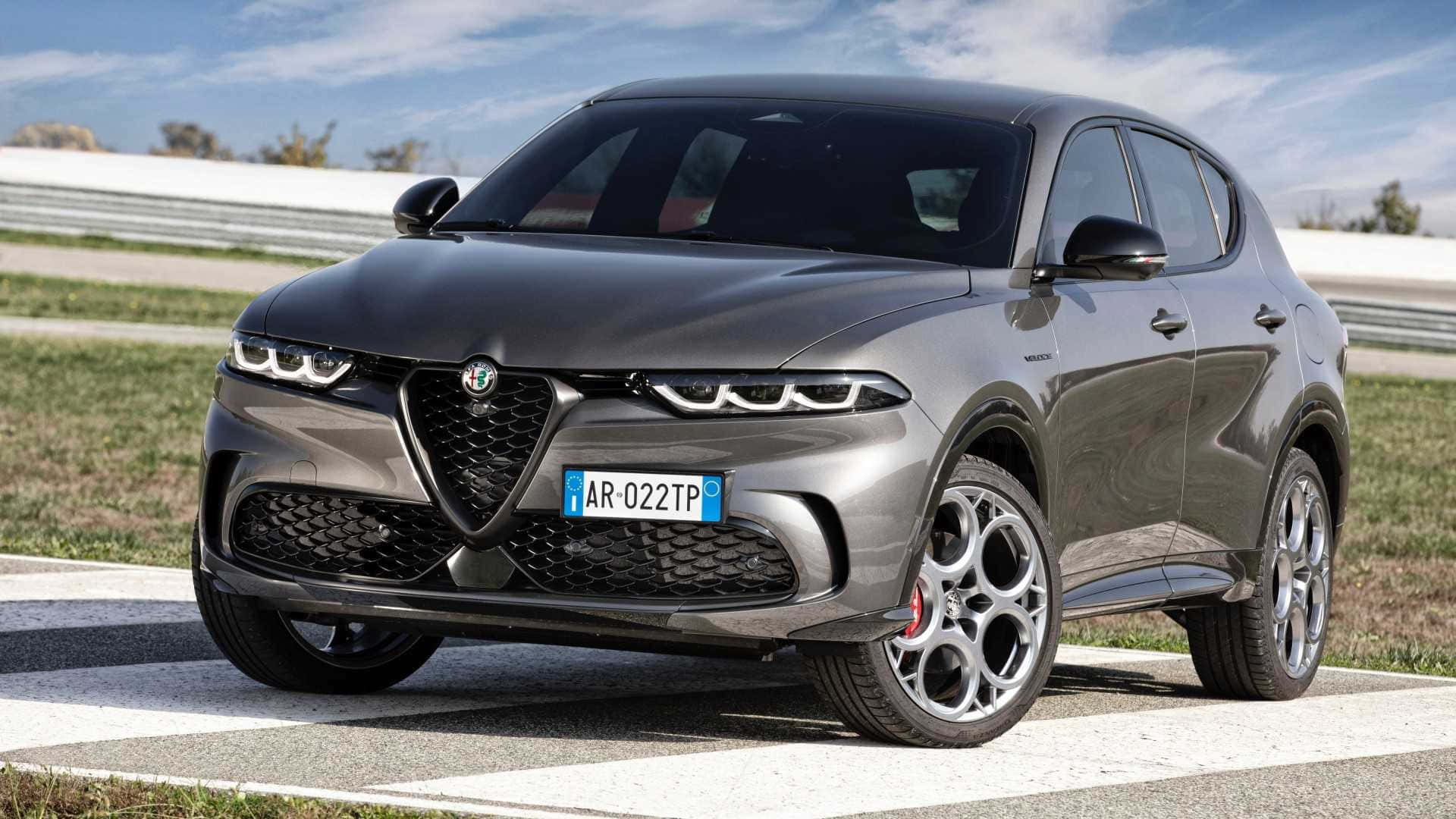愛快羅密歐 桌布 壁紙 — 一輛時尚的灰色Alfa Romeo SUV停泊在賽車場上，背景是晴朗的藍天和白色護欄。