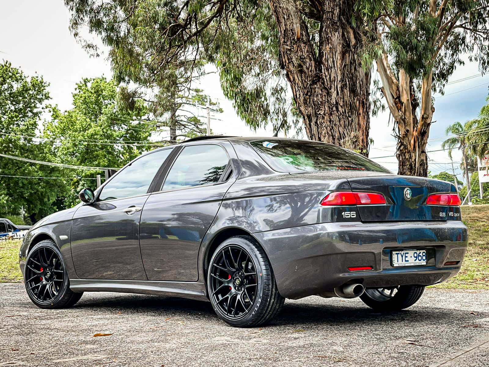 Alfa Romeo 156 桌布 壁紙 — 一輛時尚的灰色Alfa Romeo 156轎車配黑色輪圈，停在碎石路面上的茂密樹蔭下。