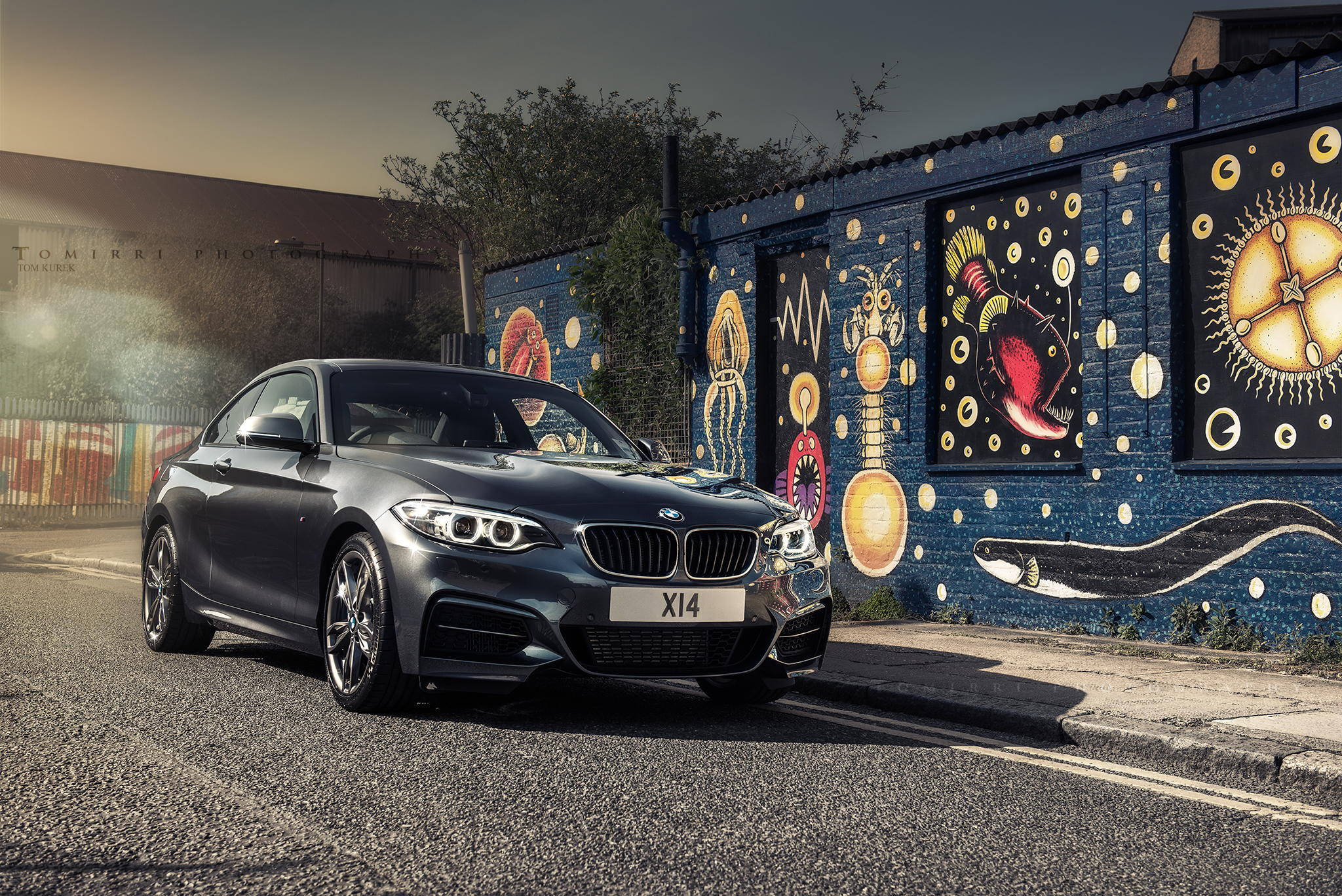 BMW 動圖 桌布 壁紙 — 一輛時尚的灰色BMW X14轎跑車停泊在瀝青街道上，旁邊是充滿活力的藍色塗鴉牆，上面有宇宙和生物壁畫。