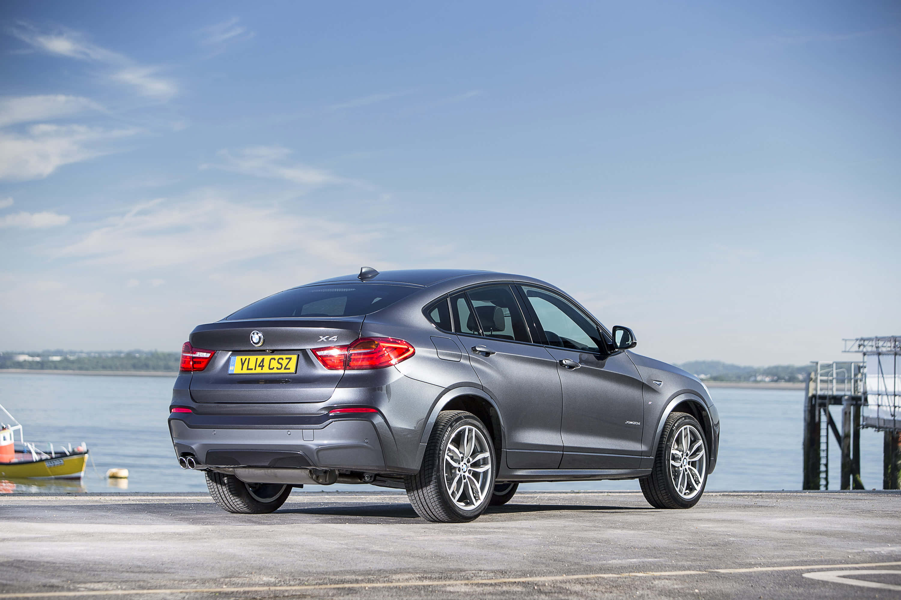 Bmw X4 桌布 壁紙 — 一輛時尚的灰色BMW X4 SUV停泊在海濱碼頭上，背景是平靜的海面和清澈的藍天。