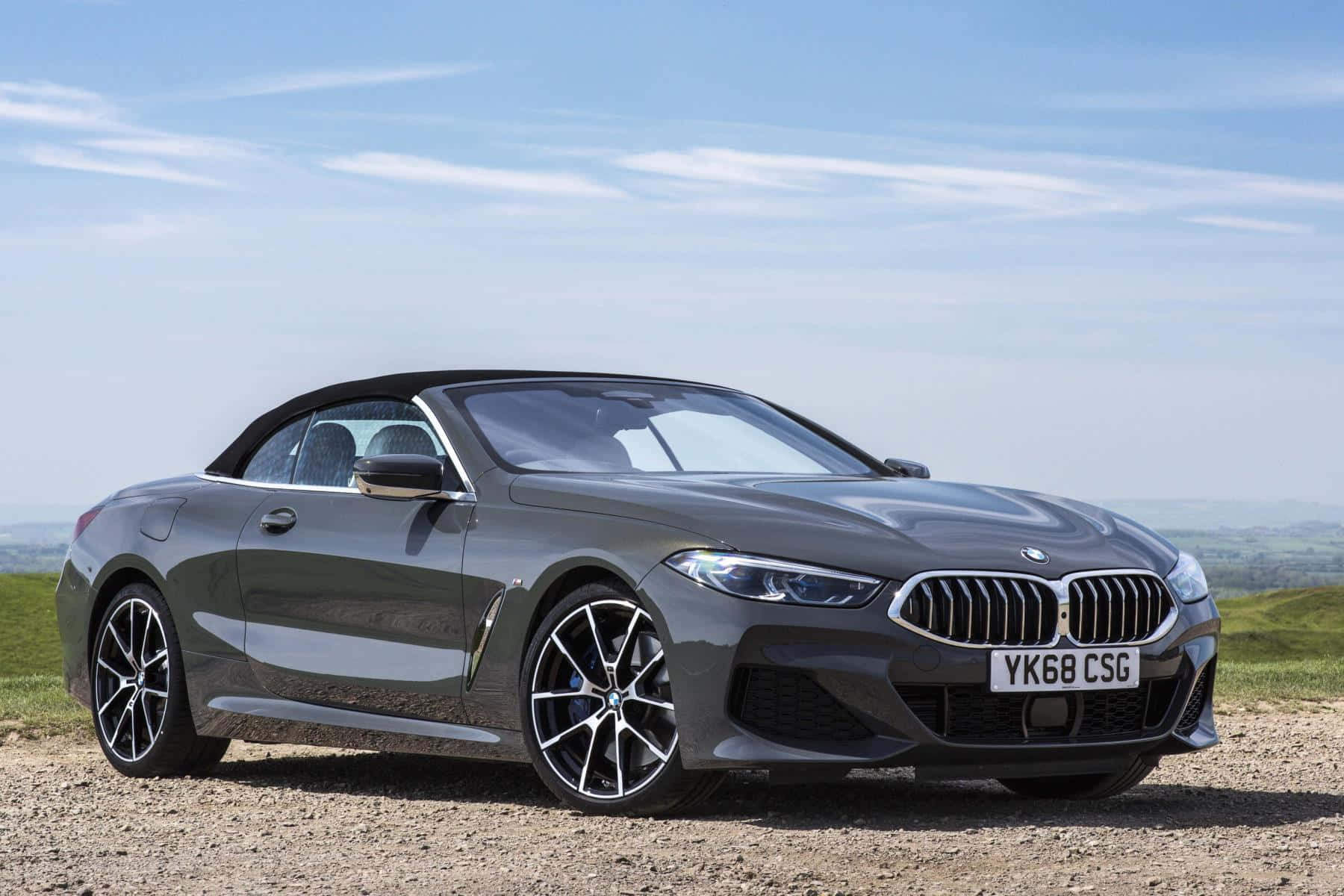 Bmw 8 Series 桌布 壁紙 — 一輛時尚的灰色BMW敞篷車停泊在碎石山坡上，天空湛藍，白雲點點。
