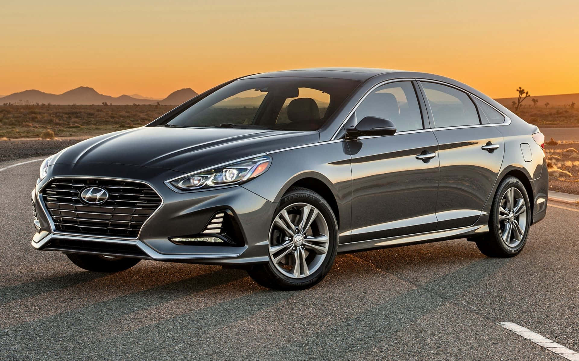 Hyundai Azera 桌布 壁紙 — 一輛時尚的灰色Hyundai Sonata轎車在金色日落時分的沙漠公路上閃耀，遠山相伴。