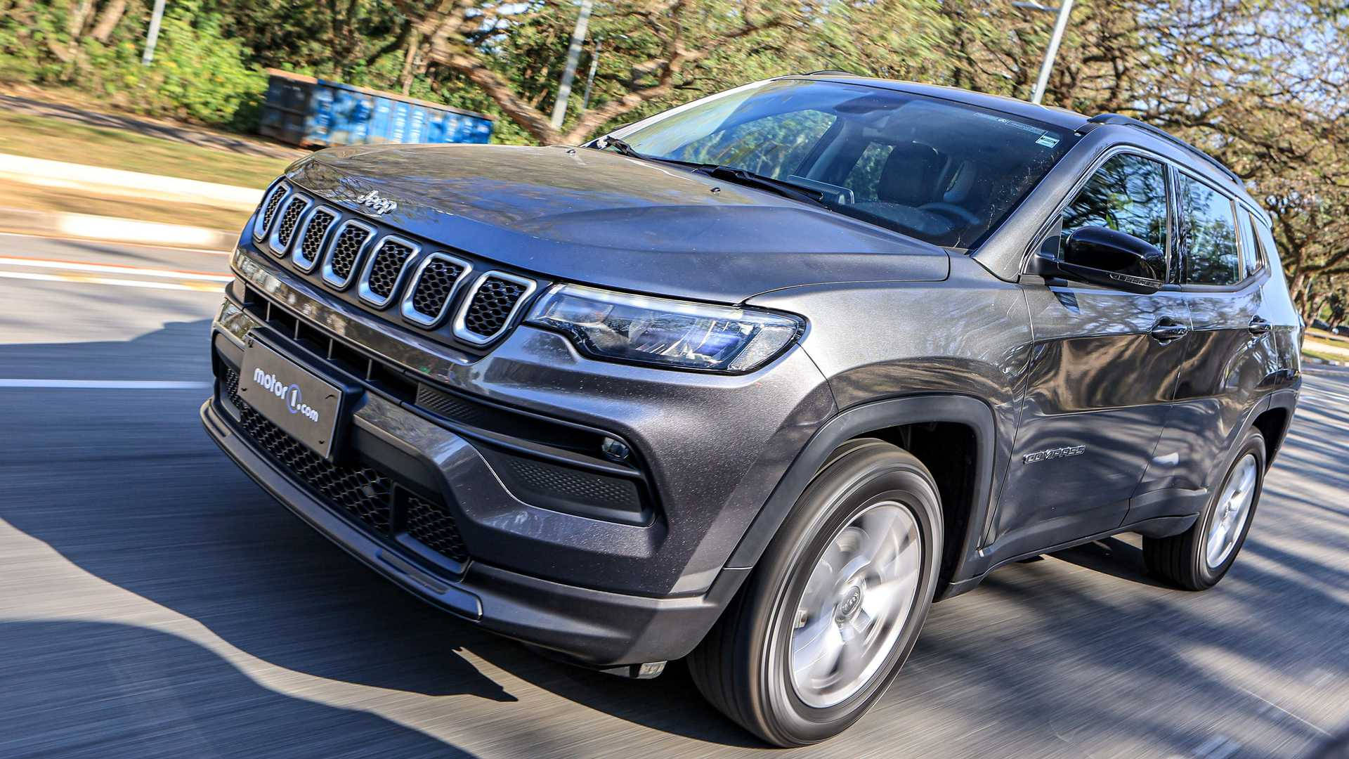 driving 桌布 壁紙 — 一輛時尚的灰色Jeep Compass在陽光明媚的道路上行駛，背景是模糊的樹木和護欄。