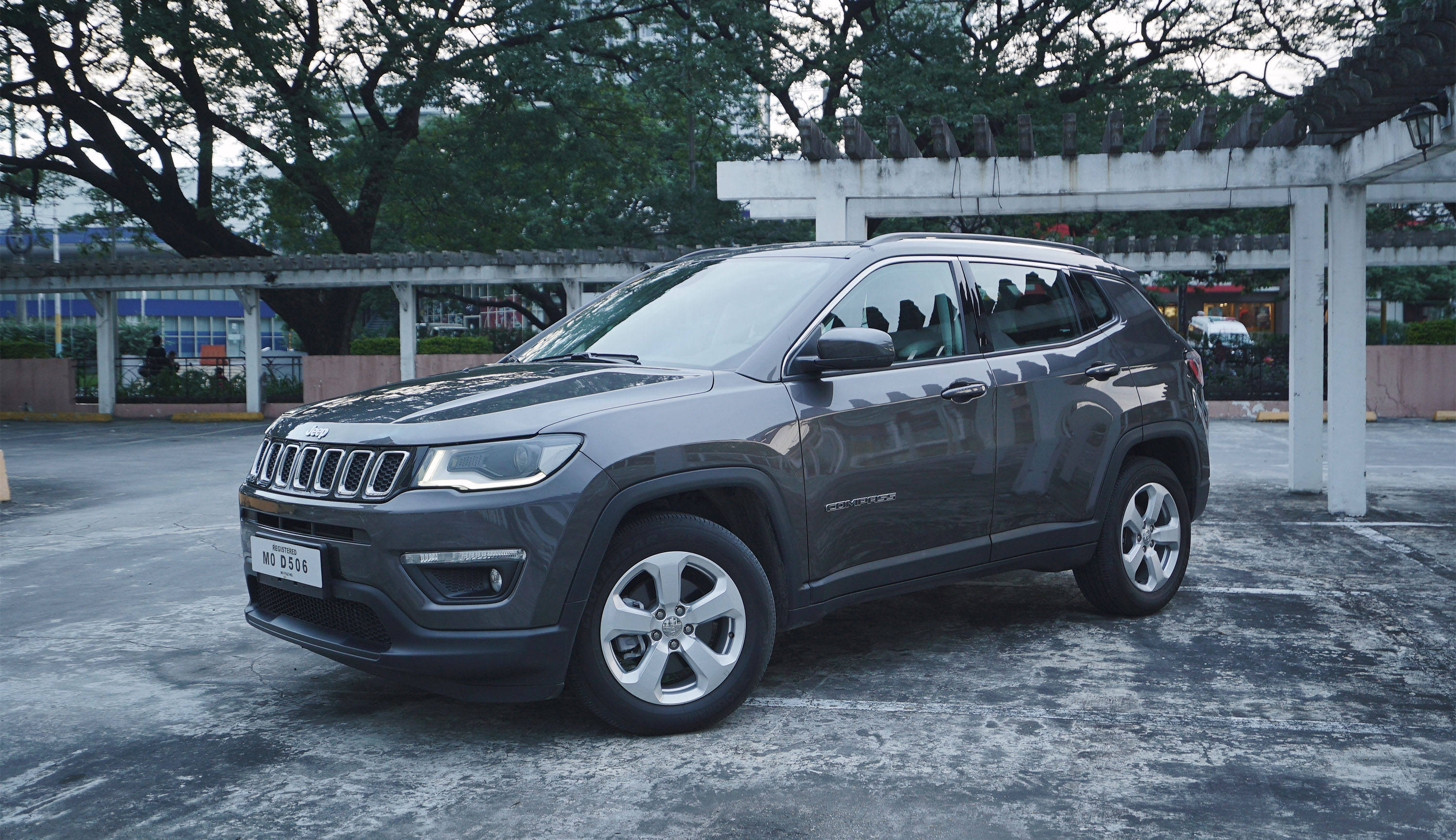 混凝土 桌布 壁紙 — 一輛時尚的灰色Jeep Compass SUV停泊在樹蔭下的鋪砌停車場，環境光線柔和。