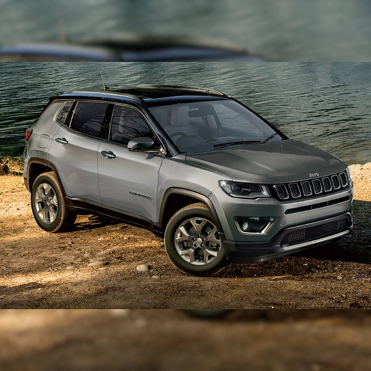 水 桌布 壁紙 — 一輛時尚的灰色Jeep Compass停泊在陽光照耀的泥土岸邊，旁邊是平靜的水面。