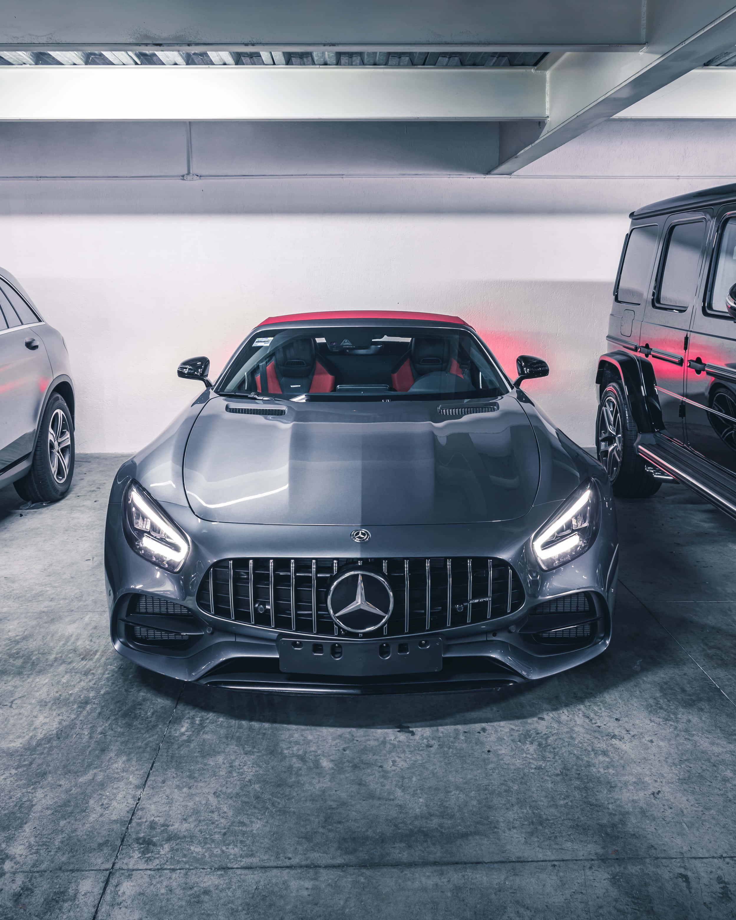 Black Car 桌布 壁紙 — 一輛時尚的灰色Mercedes-AMG GT帶有紅色點綴，在涼爽的車庫燈光下與其他豪華車輛並排閃耀。