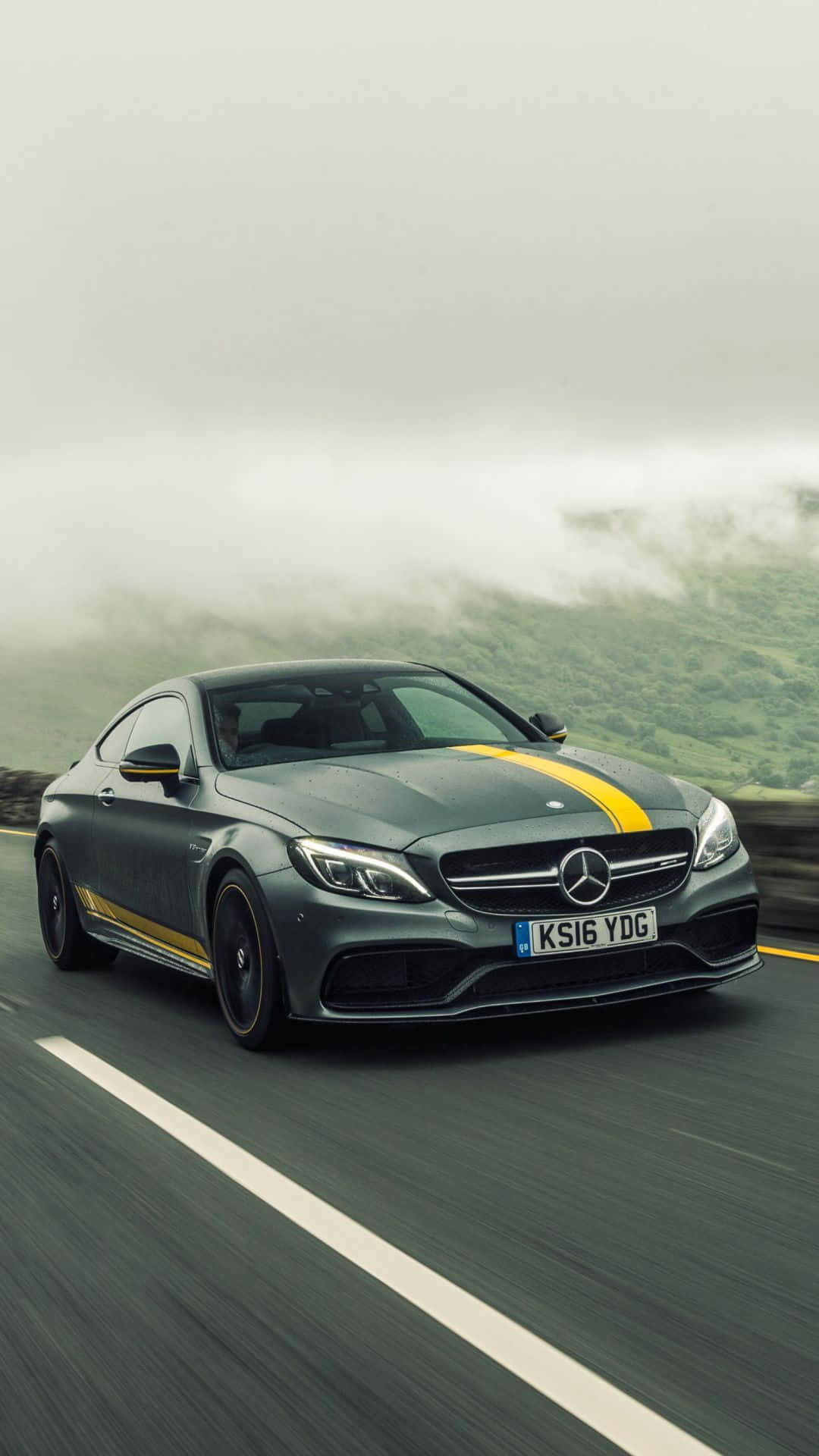汽車 桌布 壁紙 — 一輛時尚的灰色Mercedes-AMG C63 Coupe帶有黃色賽車條紋，在霧氣瀰漫的山路上疾馳。
