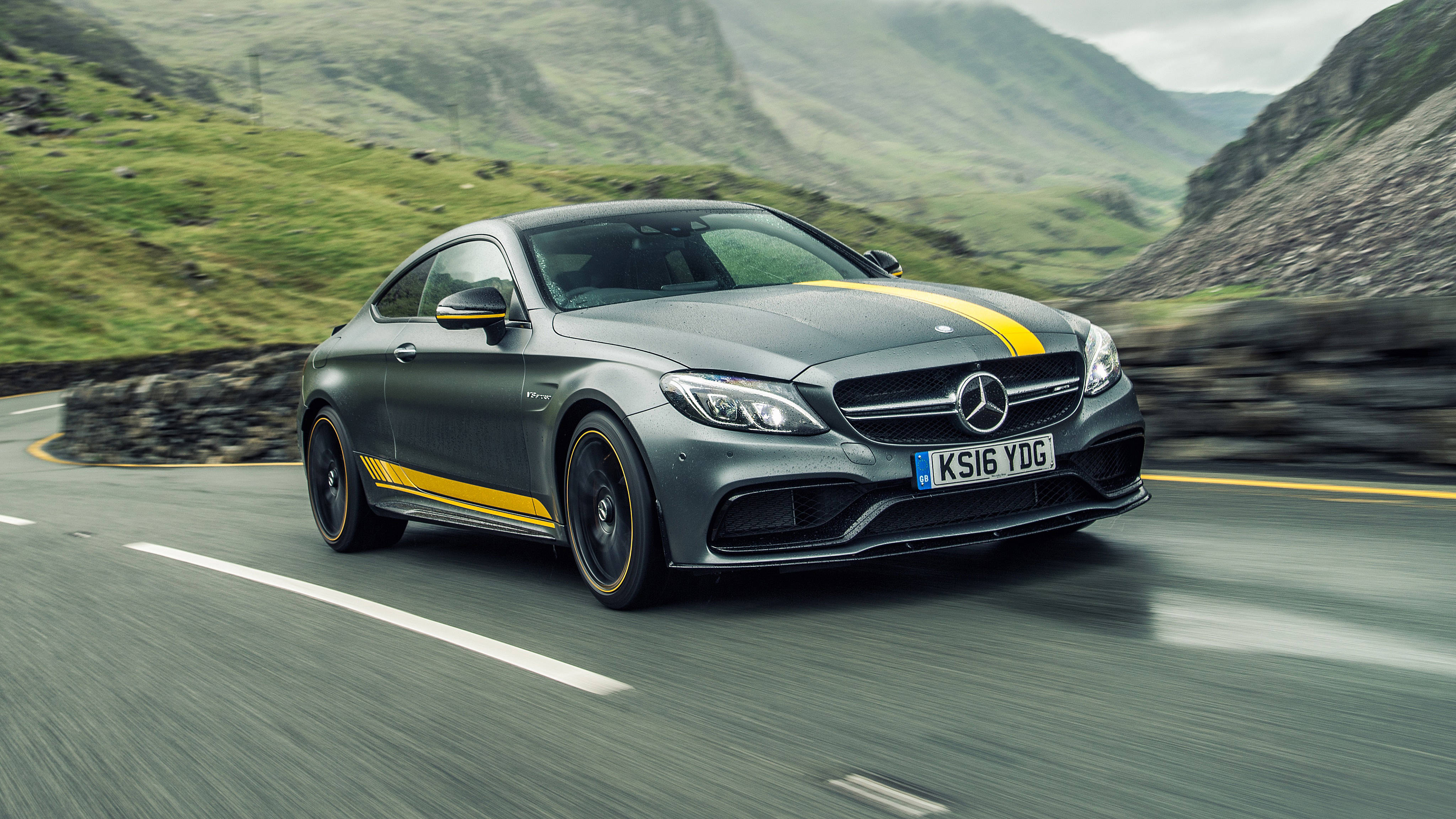 benz 4K 桌布 壁紙 — 一輛時尚的灰色Mercedes-AMG C63 Coupe帶有黃色賽車條紋，沿著蜿蜒的山路飛馳。