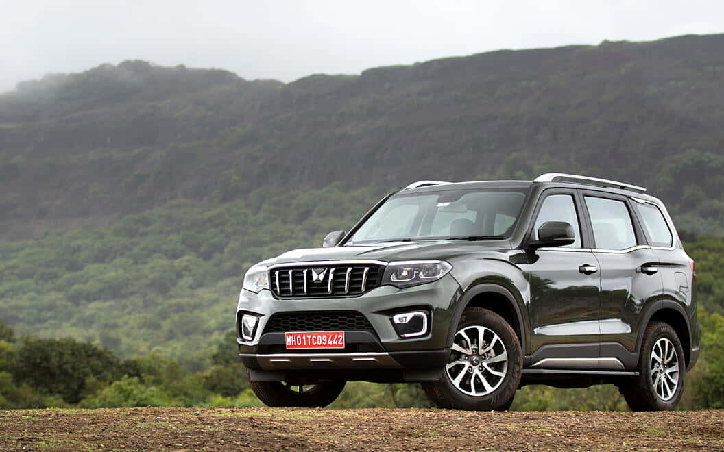 Mahindra Scorpio 桌布 壁紙 — 一輛時尚的灰色SUV停泊在泥土路上，背景是翠綠的山丘和霧氣繚繞的山脈。