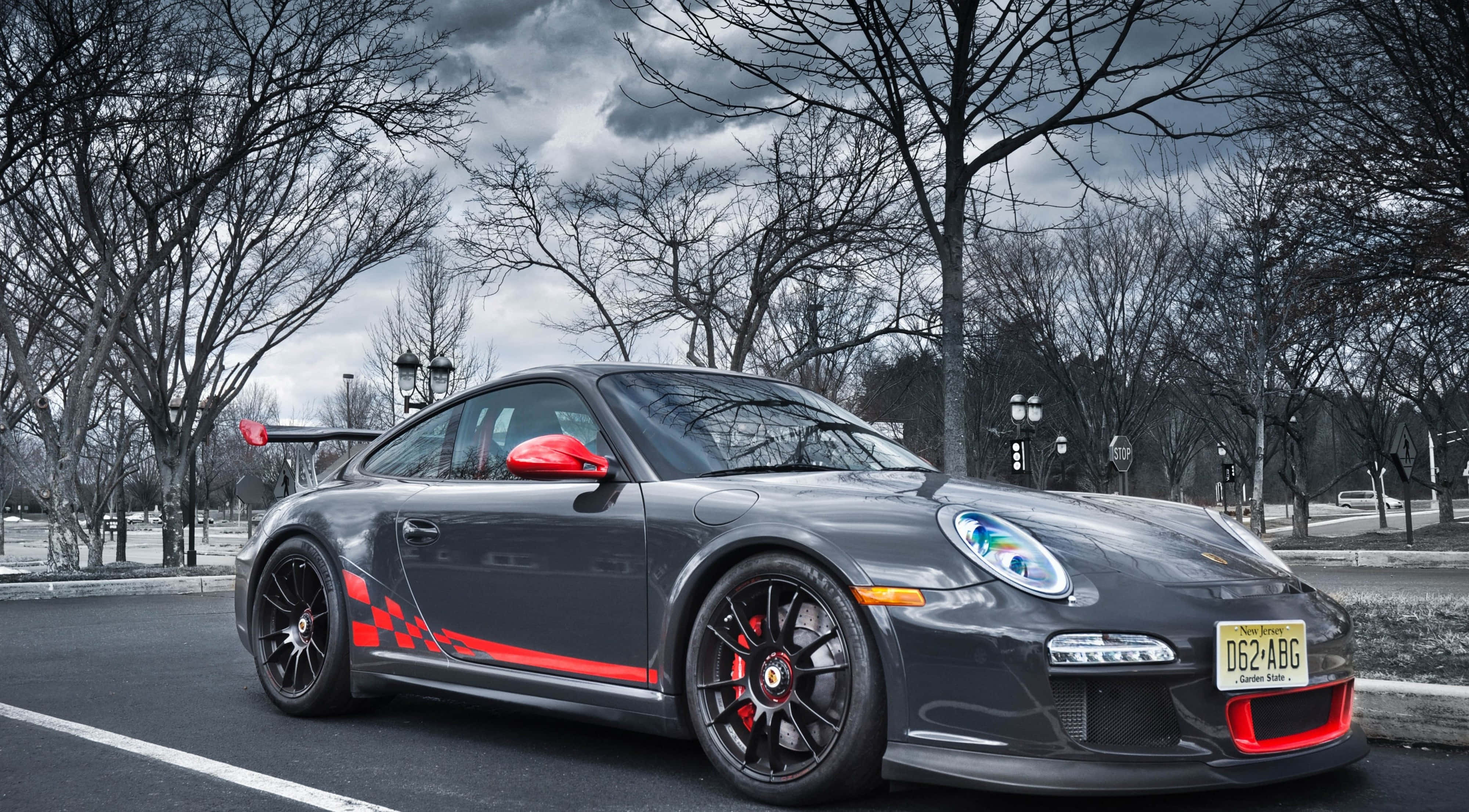 桌布 壁紙 — 一輛時尚的灰色保時捷911 GT3 RS，帶有醒目的紅色點綴，停在瀝青路上，天空陰沉多雲，樹木光禿。
