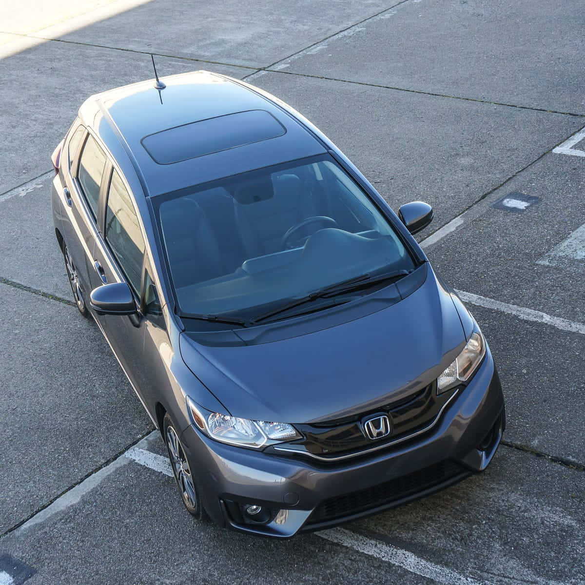 Honda Fit 桌布 壁紙 — 一輛時尚的灰色本田Fit停放在陽光普照的混凝土停車場，地上有白色標線。