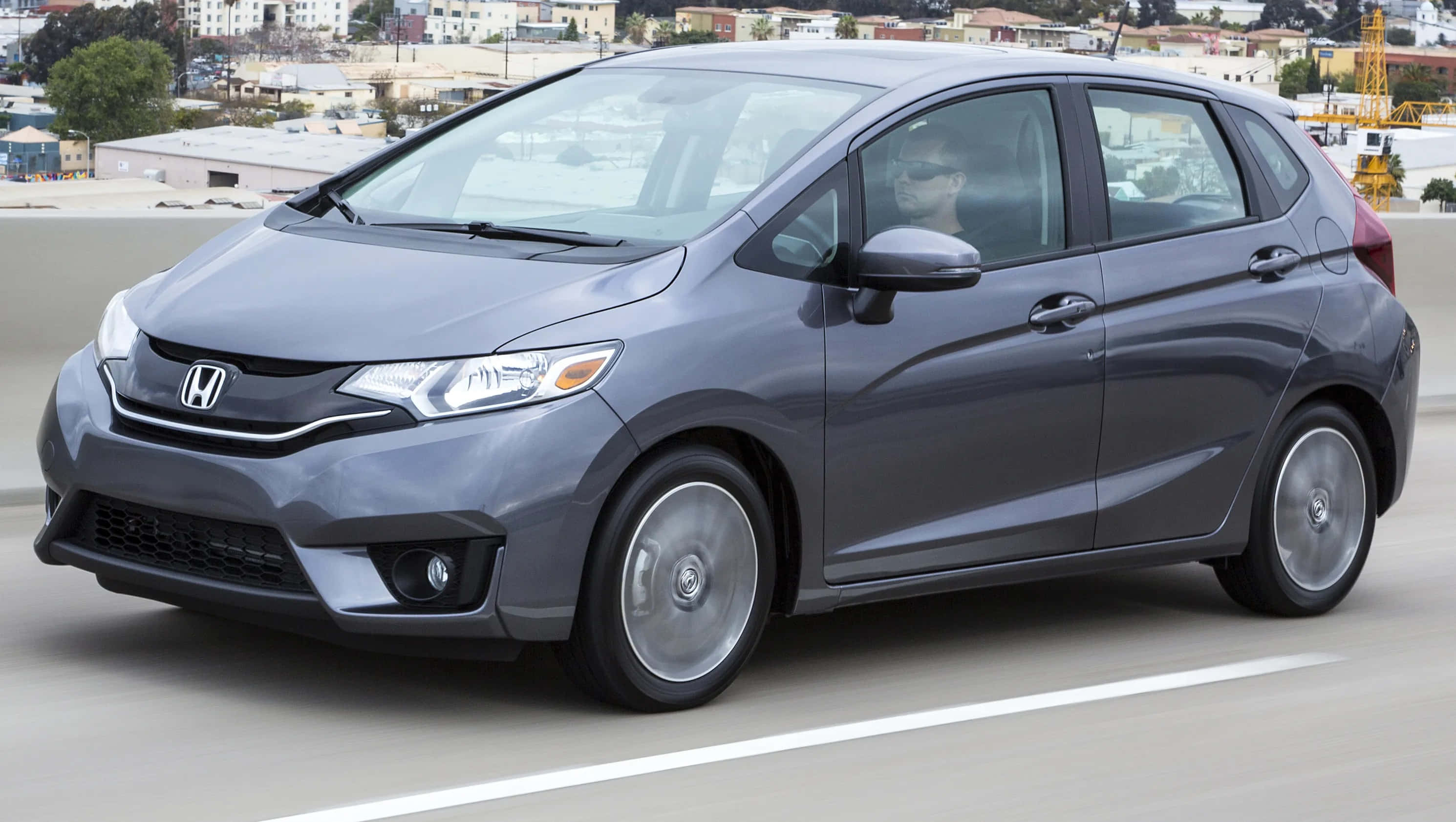 Compact Car 桌布 壁紙 — 一輛時尚的灰色本田Fit在高速公路上行駛，背景是城市天際線。