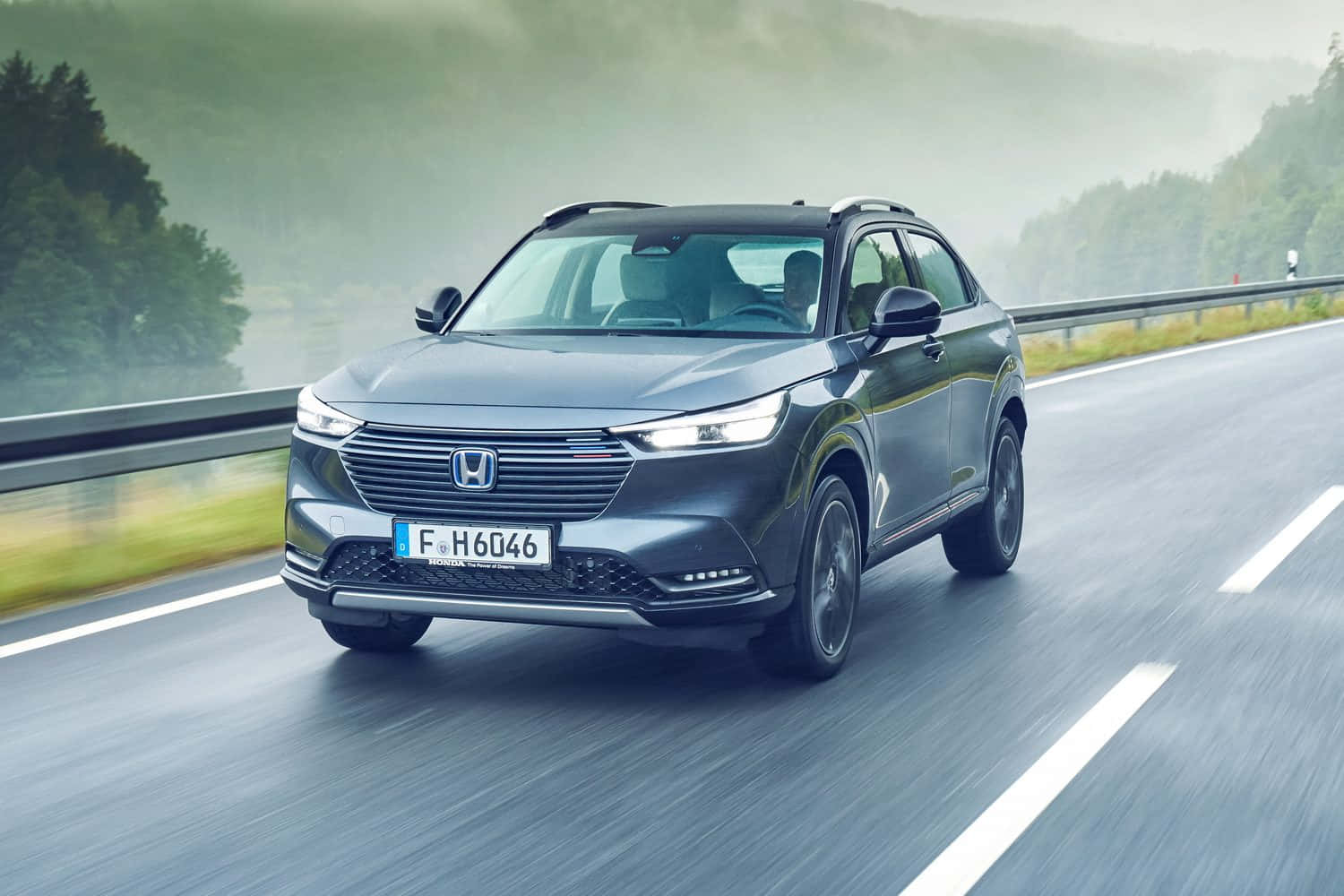 Honda Hr-v 桌布 壁紙 — 一輛時尚的灰色本田SUV在霧氣瀰漫的山區高速公路上行駛，帶有模糊的動感，兩旁是茂密的綠樹。