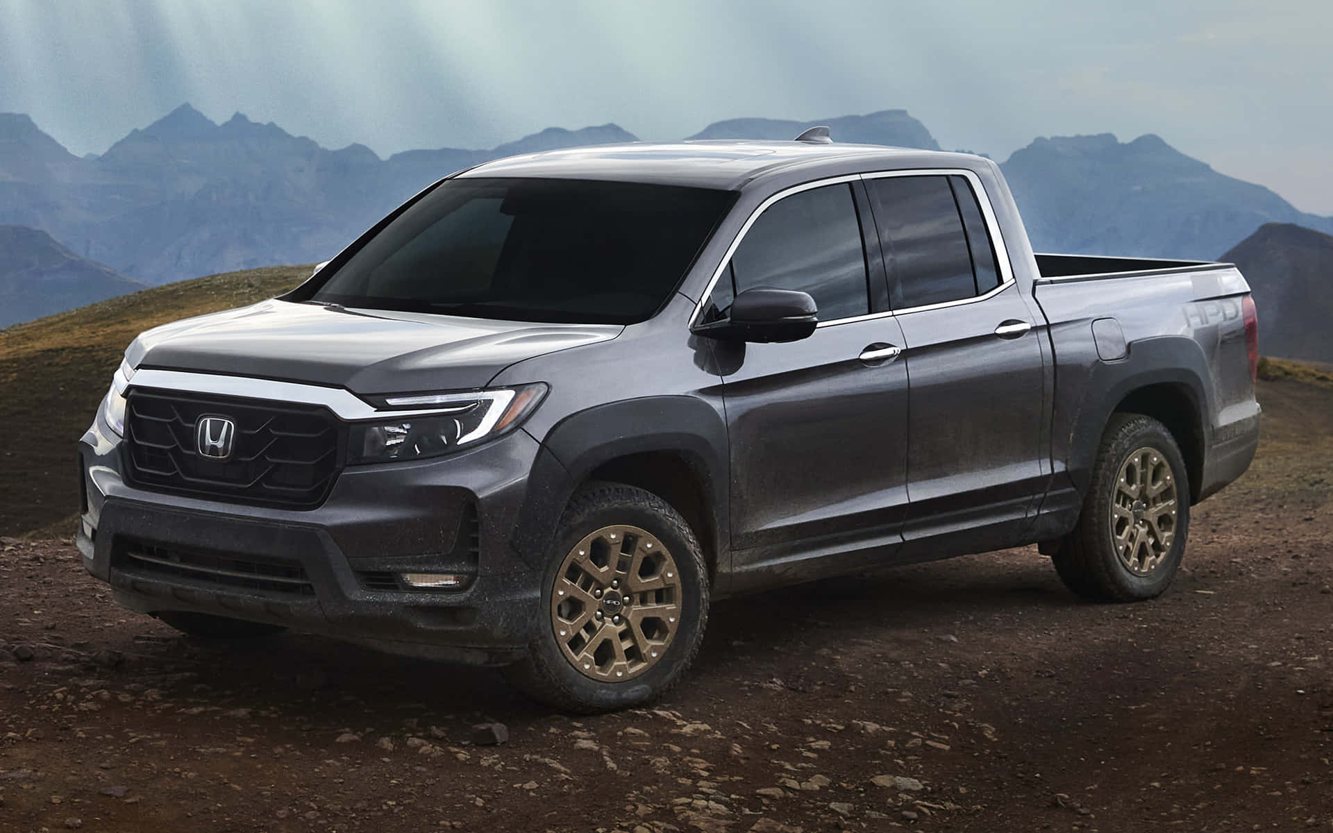 Honda Ridgeline 桌布 壁紙 — 一輛時尚的灰色本田皮卡車停在崎嶇的泥路上，背景是霧濛濛的山巒。
