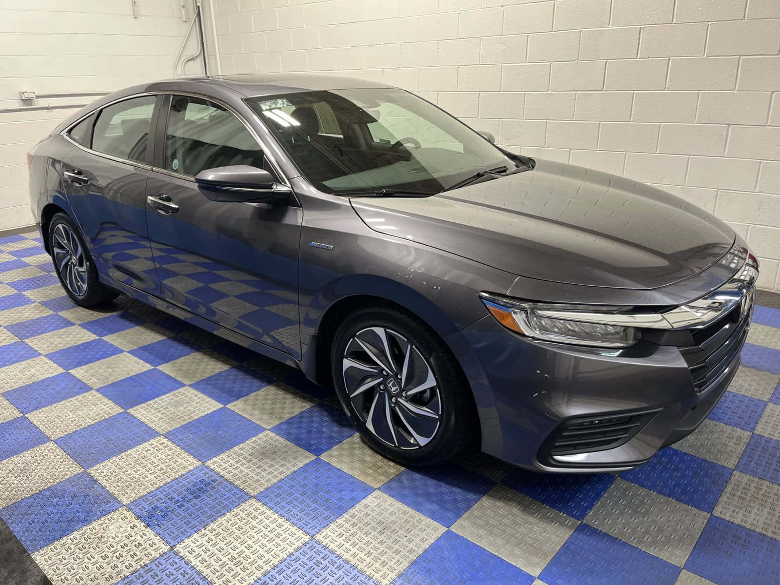 Honda Insight 桌布 壁紙 — 一輛時尚的灰色本田轎車在明亮的燈光下，在藍銀相間的格子地板上閃閃發光，背景是白色磚牆。