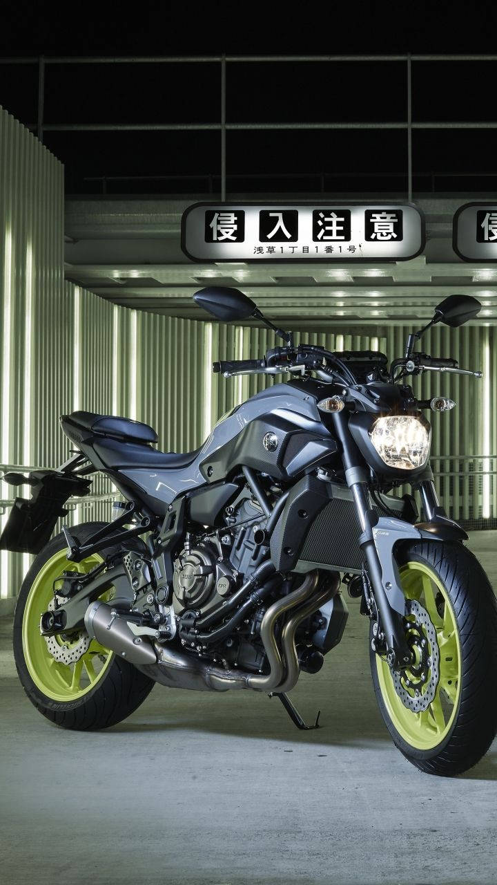 yamaha mt 15 桌布 壁紙 — 一輛時尚的灰色機車，配備螢光綠色車輪，夜晚停泊在現代工業車庫中發光的標誌下。