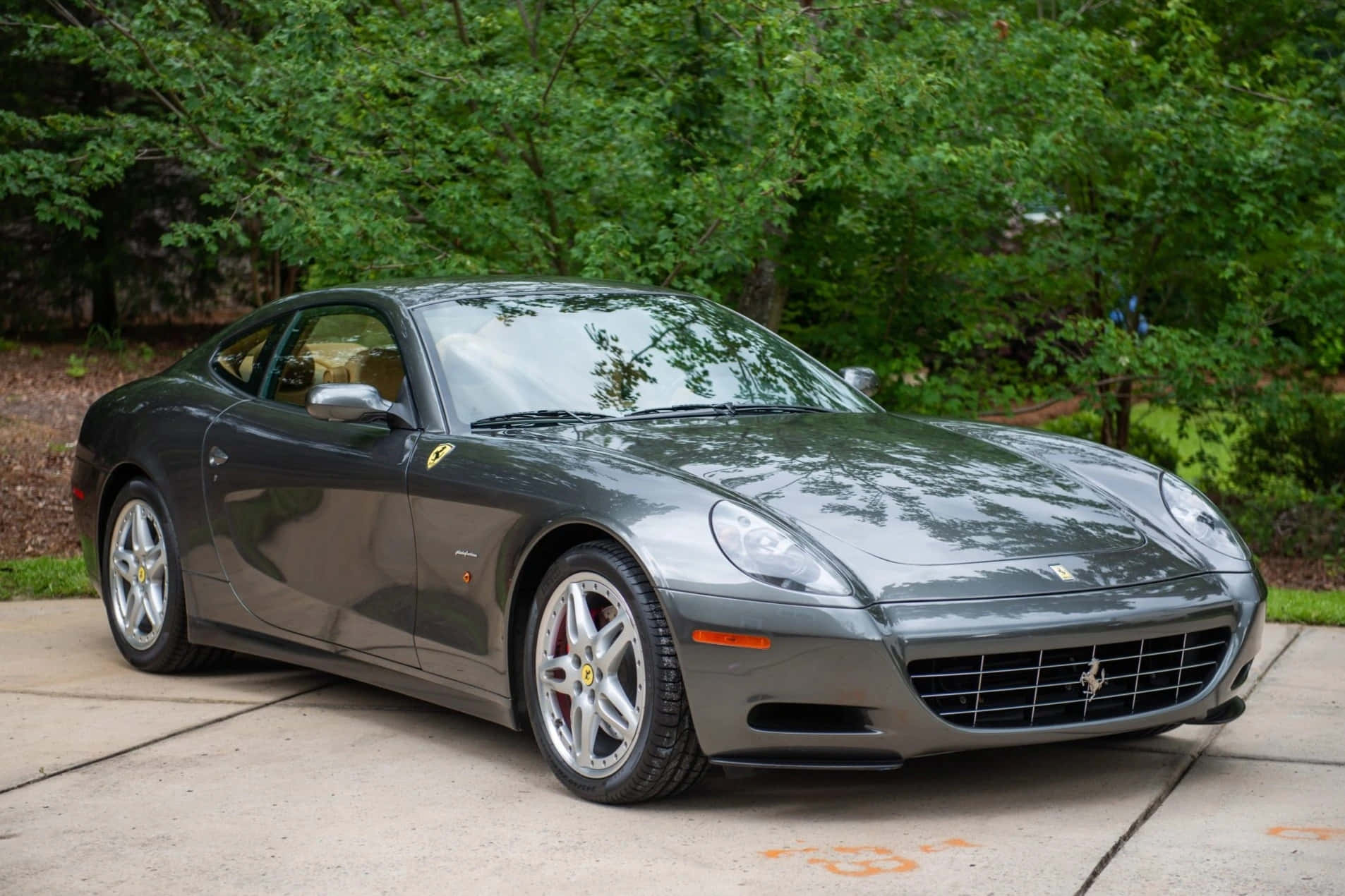 Ferrari 612 Scaglietti 桌布 壁紙 — 一輛時尚的灰色法拉利 612 Superamerica 停在混凝土車道上，周圍環繞著茂密的綠樹。