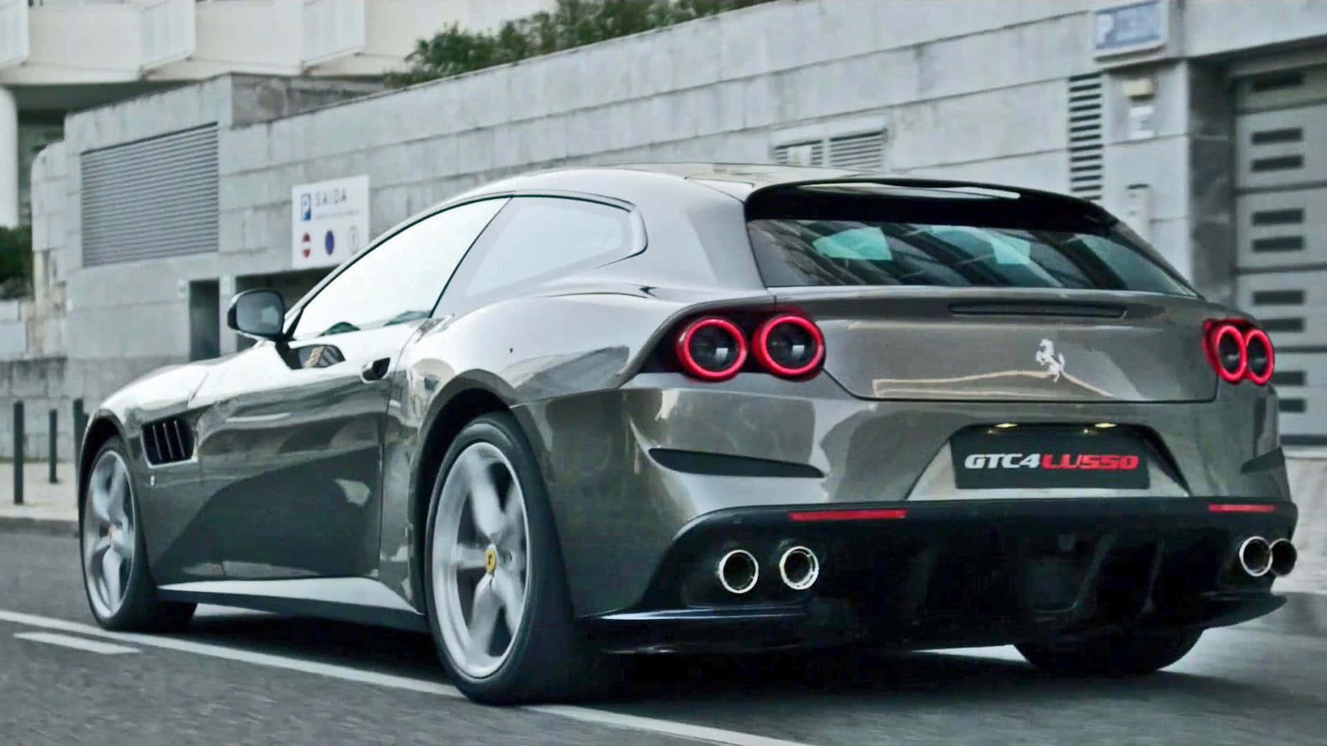 Ferrari Gtc4lusso 桌布 壁紙 — 一輛時尚的灰色法拉利 GTC4Lusso 跑車，帶有紅色尾燈，停在混凝土建築附近的城市街道上。