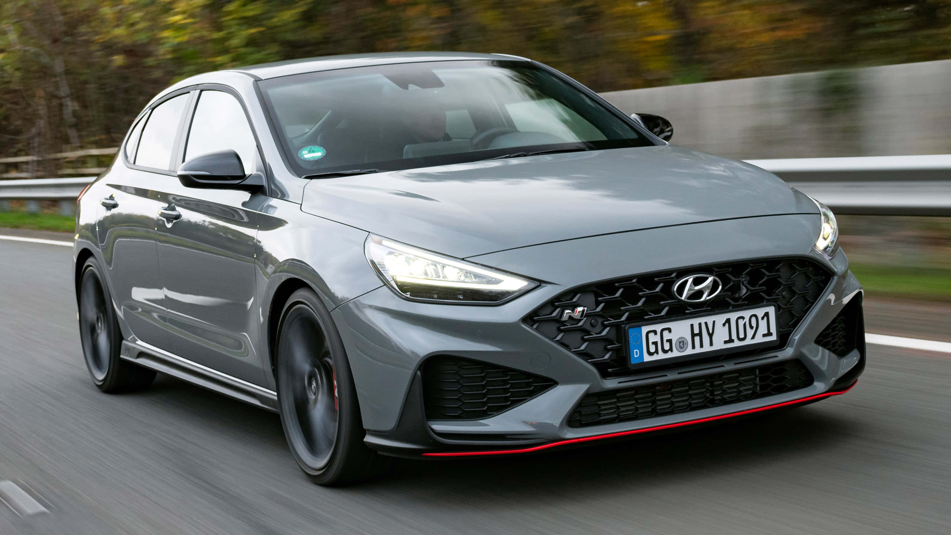 Hyundai 桌布 壁紙 — 一輛時尚的灰色現代 i30 N 掀背車沿著蜿蜒的道路飛馳，背景是模糊的秋樹。