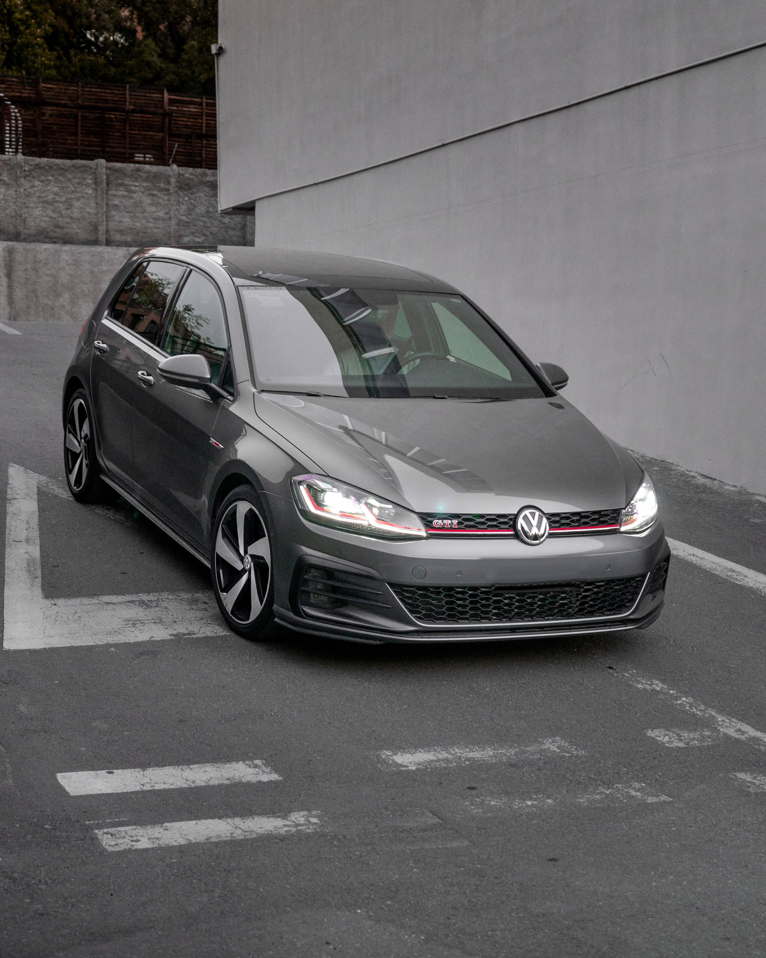 Gti 桌布 壁紙 — 一輛時尚的灰色福斯 Golf GTI 停放在混凝土停車場，地上有白色標線，背景為簡約的城市景觀。