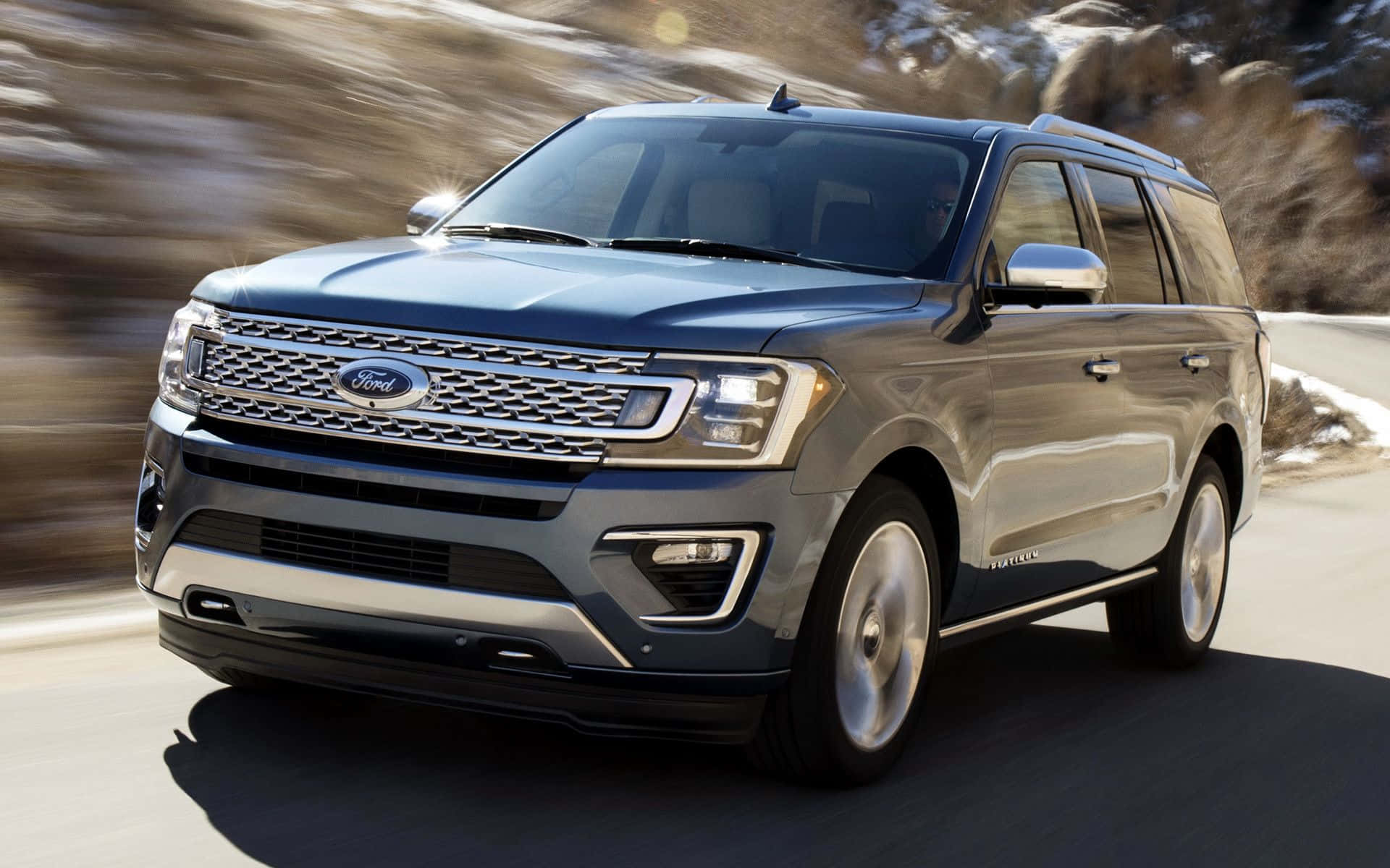 Ford Expedition 桌布 壁紙 — 一輛時尚的灰色福特Expedition SUV在蜿蜒的山路上疾馳，背景是模糊的岩石地形。