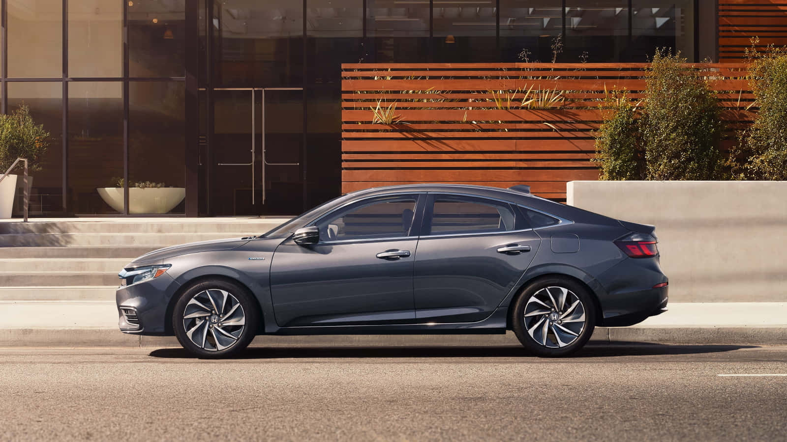 Honda Insight 桌布 壁紙 — 一輛時尚的灰色轎車停放在城市街道上，旁邊是一座帶有玻璃窗和木條的現代建築。