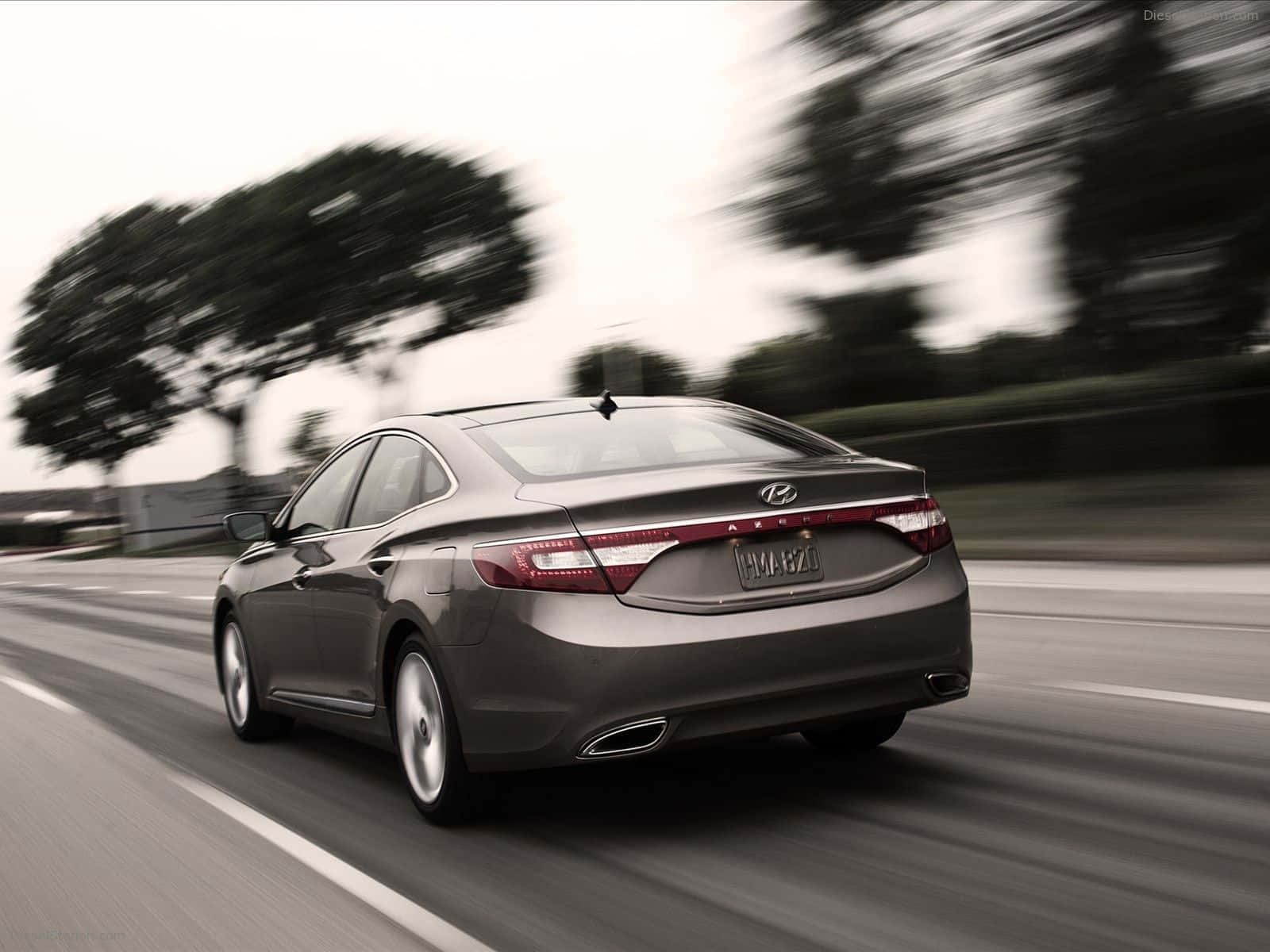 Hyundai Azera 桌布 壁紙 — 一輛時尚的灰色轎車在高速公路上疾馳，模糊的樹木和天空傳達出運動感和現代設計。