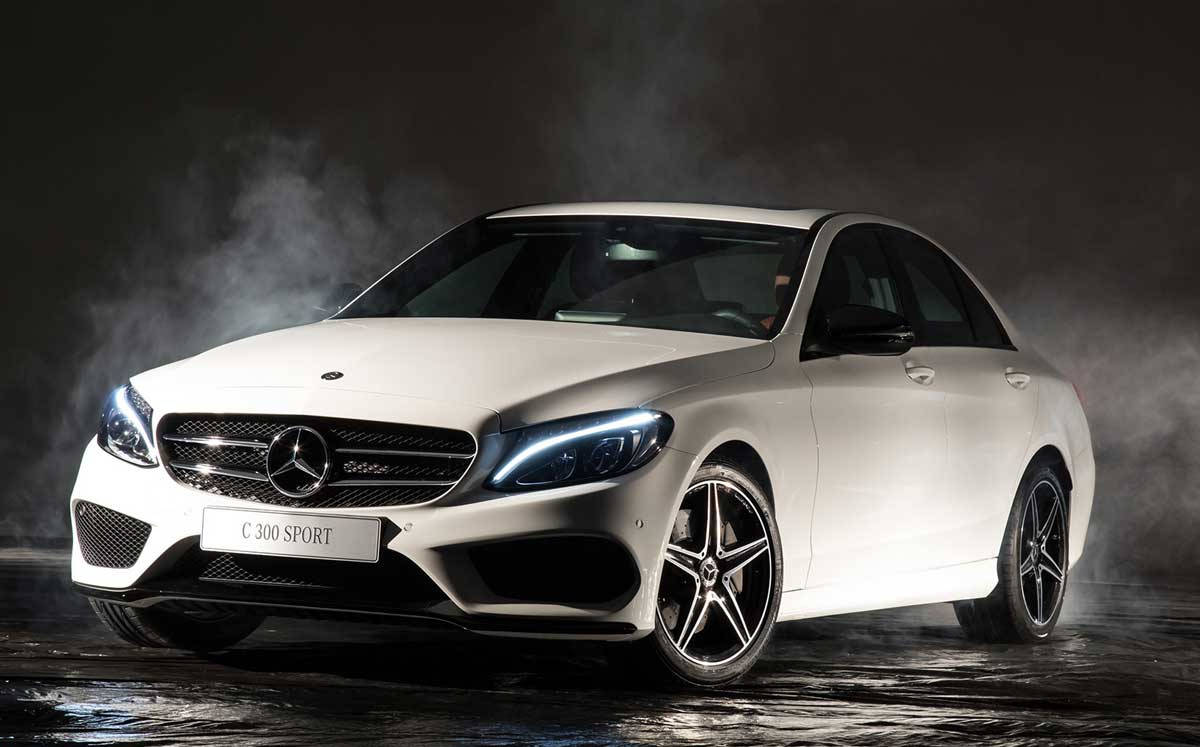 Mercedes Benz C300 桌布 壁紙 — 一輛時尚的白色 Mercedes C 300 Sport 轎車在戲劇性的攝影棚燈光下閃閃發光，煙霧在其激進的前格柵和發光的車頭燈周圍旋轉。