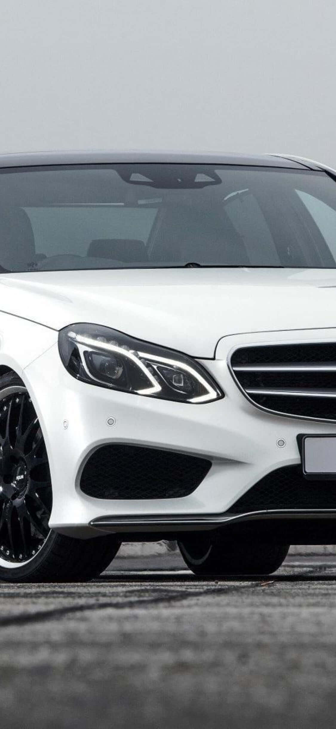Car Front View 桌布 壁紙 — 一輛時尚的白色 Mercedes-Benz 跑車配黑色輪圈，停放在灰色瀝青路面上，天空多雲。