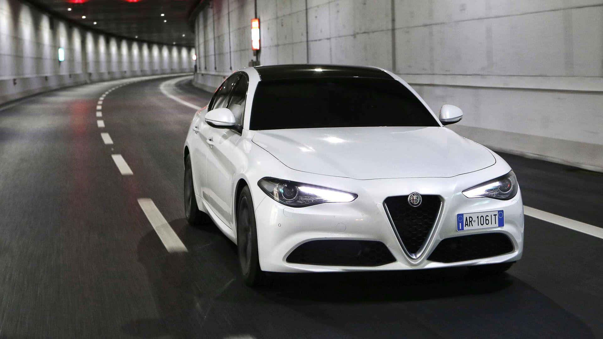 愛快羅密歐 桌布 壁紙 — 一輛時尚的白色Alfa Romeo轎車在燈光昏暗的混凝土隧道中疾馳，車頭燈閃爍。
