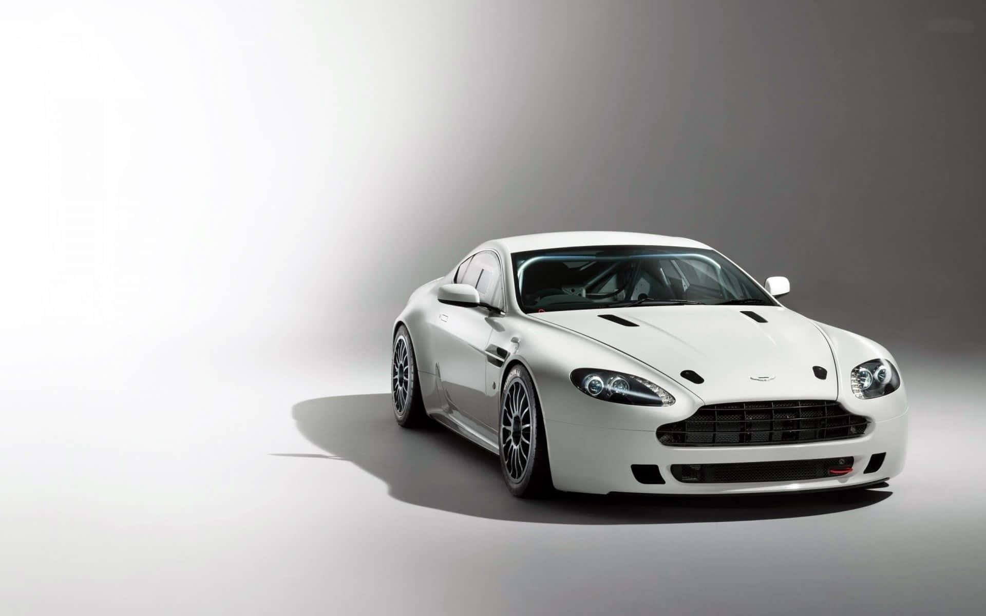 Aston Martin V12 Vantage 桌布 壁紙 — 一輛時尚的白色Aston Martin跑車在攝影棚燈光下，以極簡灰色漸層背景襯托，閃耀光芒。