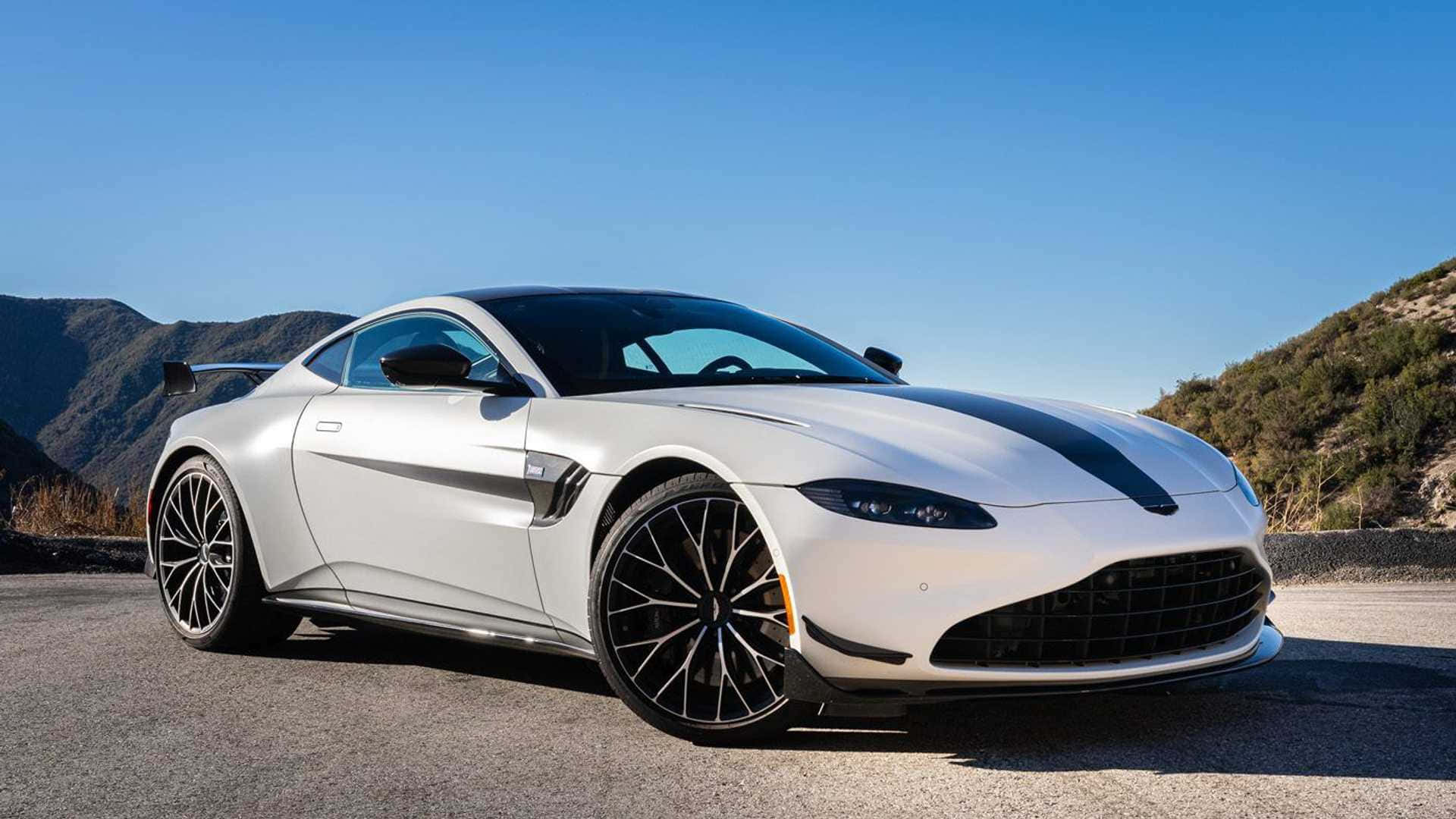 奧斯頓馬丁 桌布 壁紙 — 一輛時尚的白色Aston Martin跑車帶有黑色賽車條紋，停在藍天白雲下的山路上。