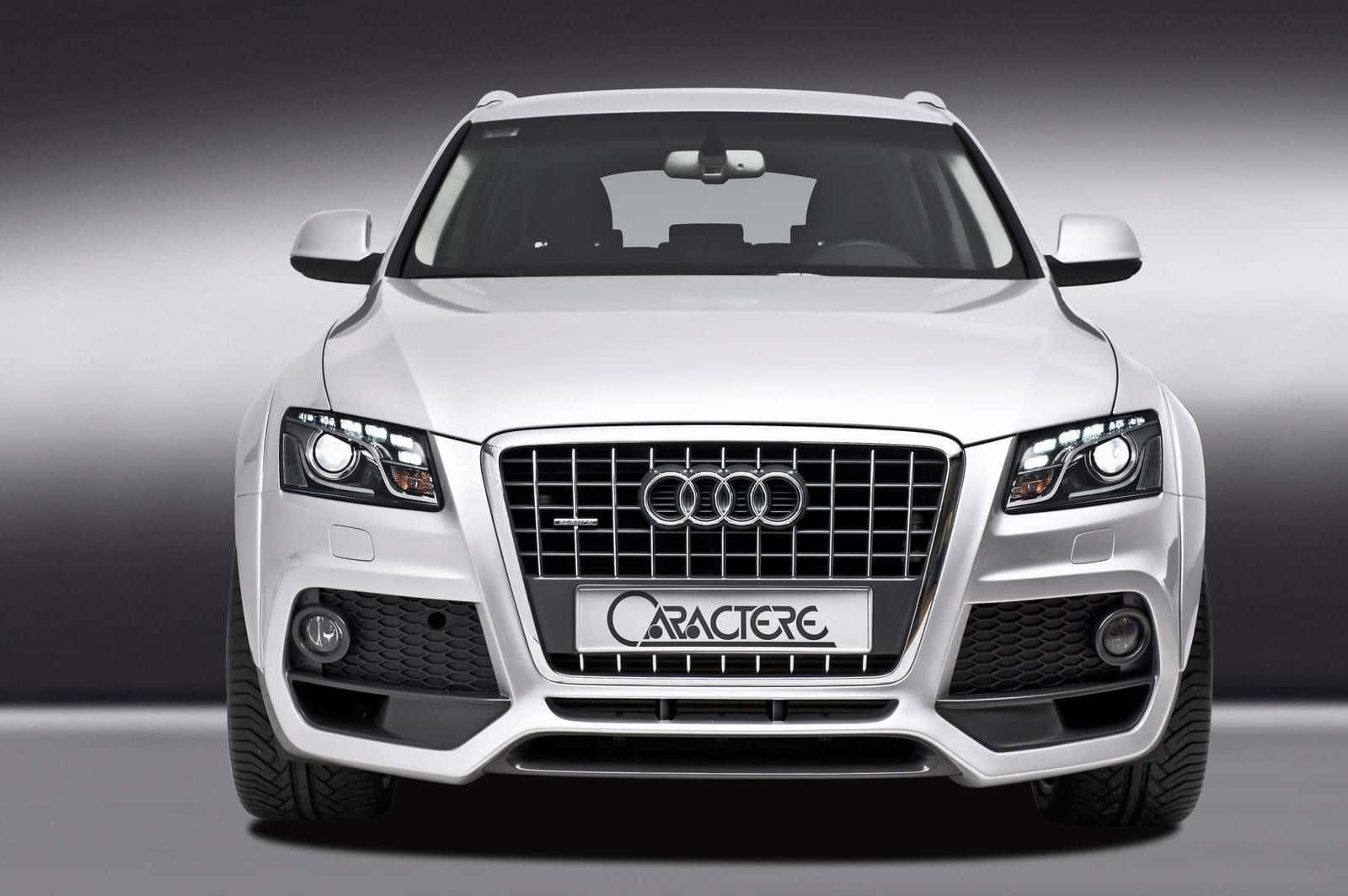Audi Sq5 桌布 壁紙 — 一輛時尚的白色Audi SUV，配備定製的Caractere水箱護罩和侵略性頭燈，在漸變灰色工作室背景前凝視前方。