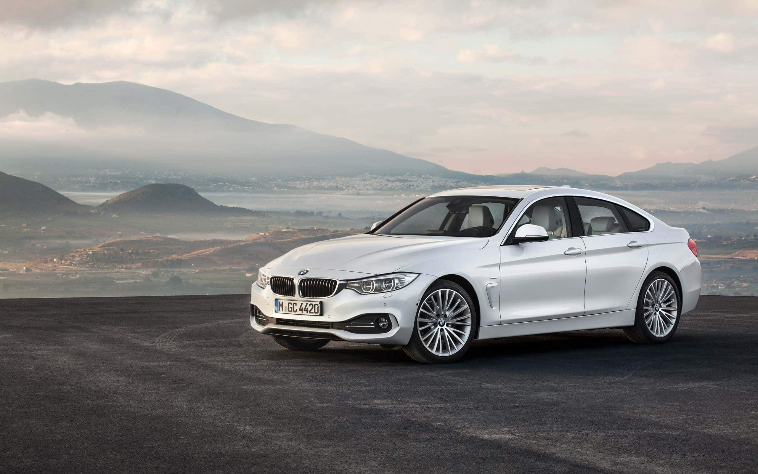 Bmw 4 Series 桌布 壁紙 — 一輛時尚的白色BMW 4系列轎跑車停在一個黑暗的觀景點，背景是霧氣繚繞的山脈和山谷，天空多雲。