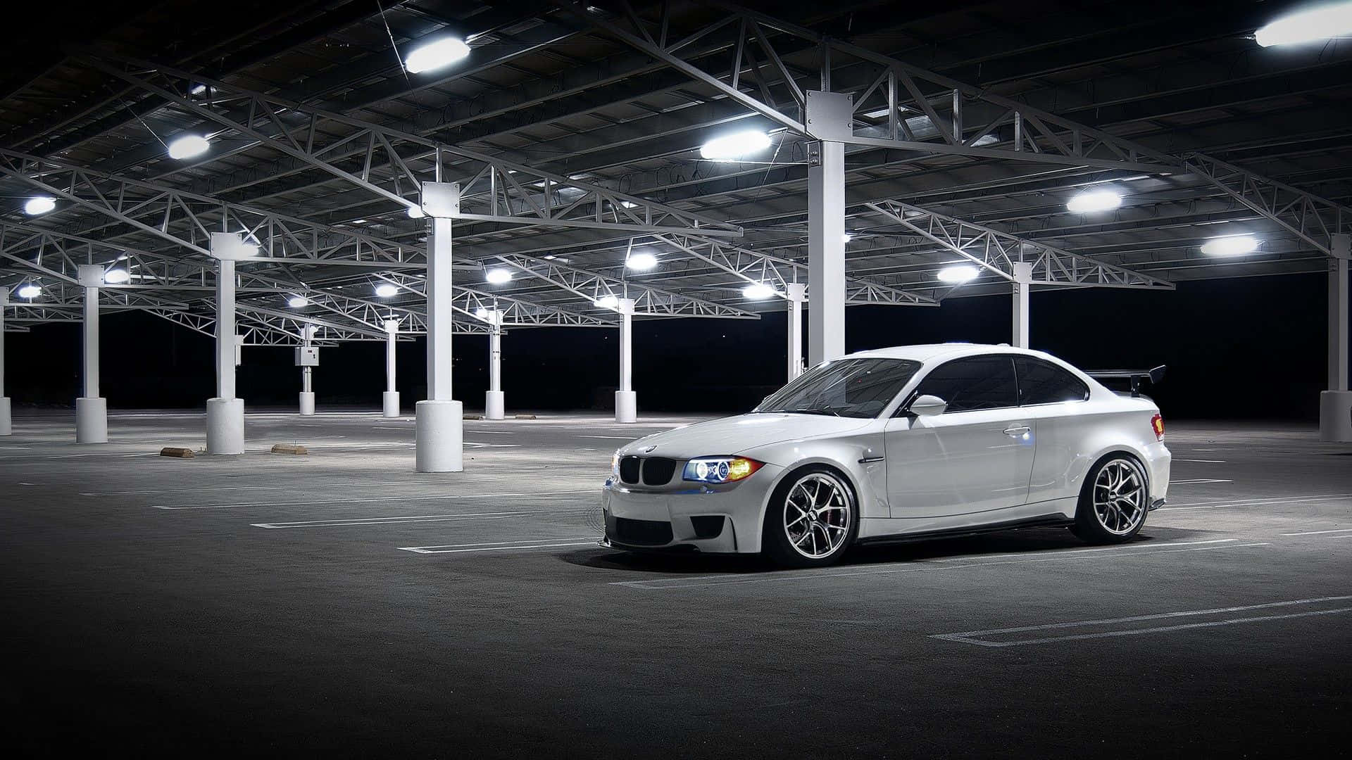 Bmw 1 Series 桌布 壁紙 — 一輛時尚的白色BMW M1跑車在夜間獨自停放在空蕩的工業車庫中，上方有明亮的頂燈。